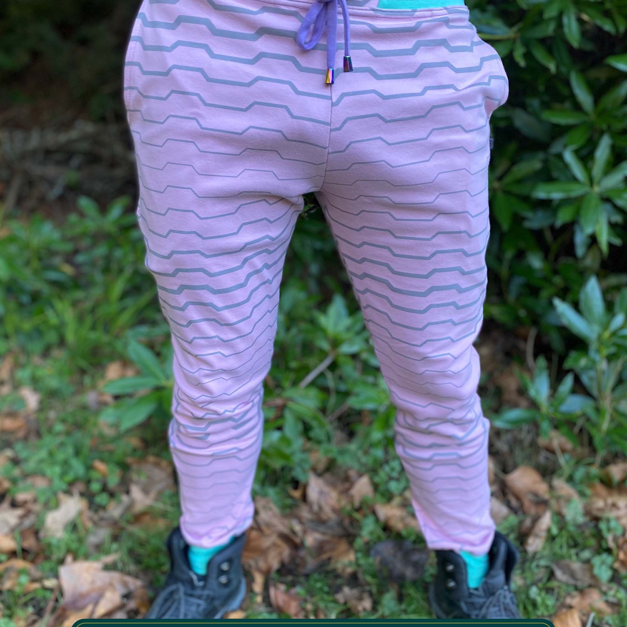 Organic cotton unisex joggers, pink fabric with geometric print and purple accents, front side view on male model in nature.