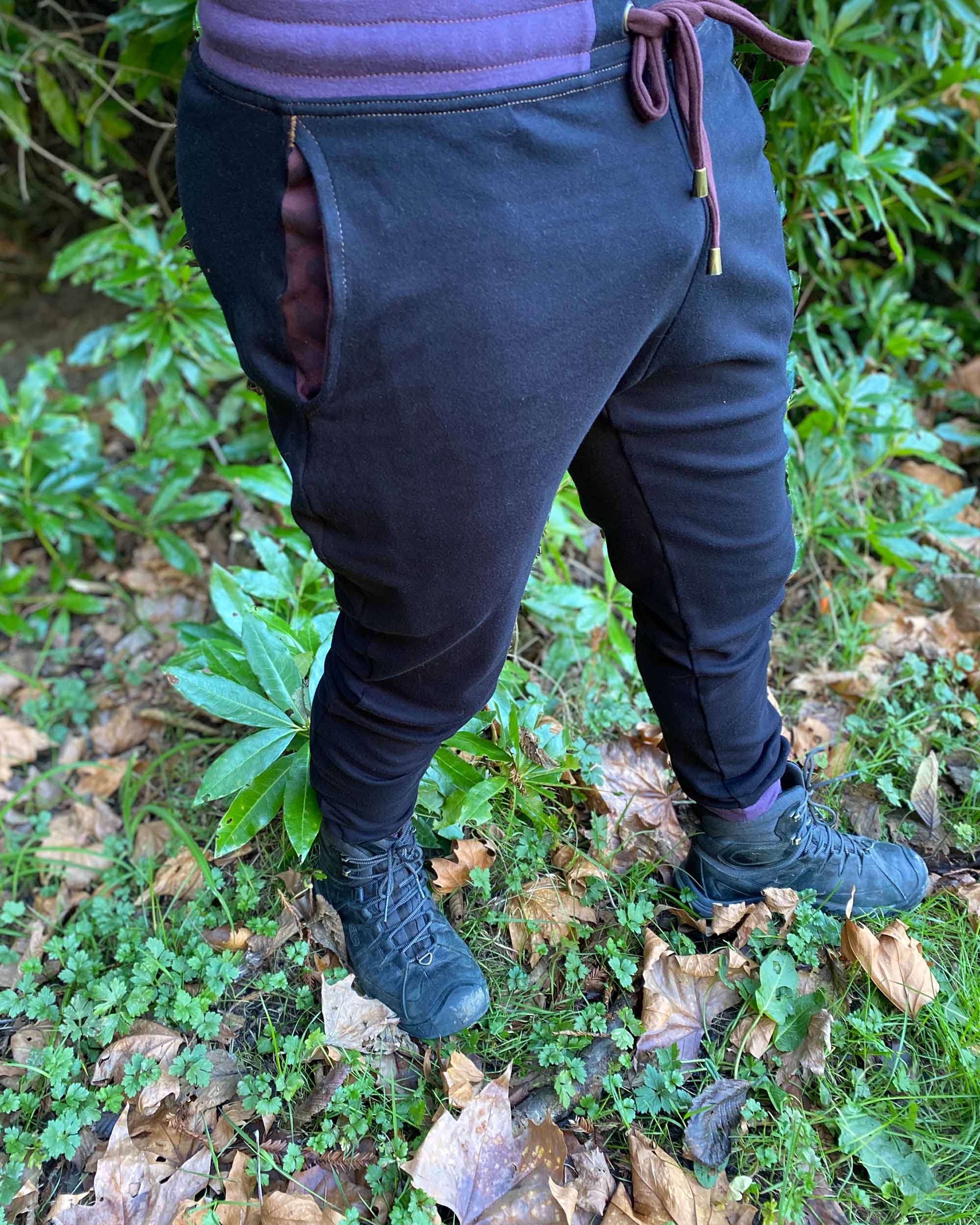 Organic cotton unisex joggers, black fabric with brown accents, right side view on male model in nature.