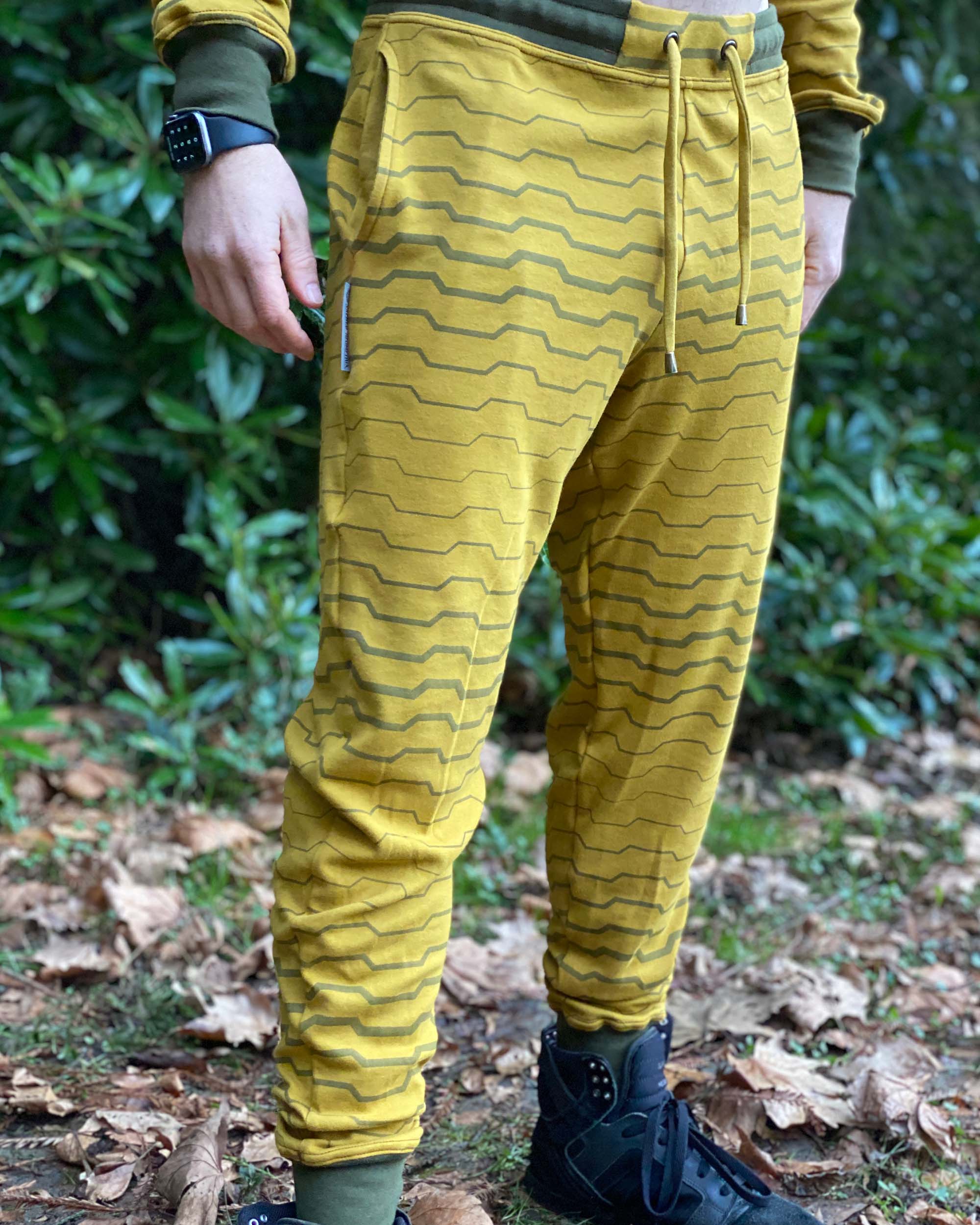 Organic cotton unisex joggers, yellow fabric with geometric print, front side view on male model in nature.