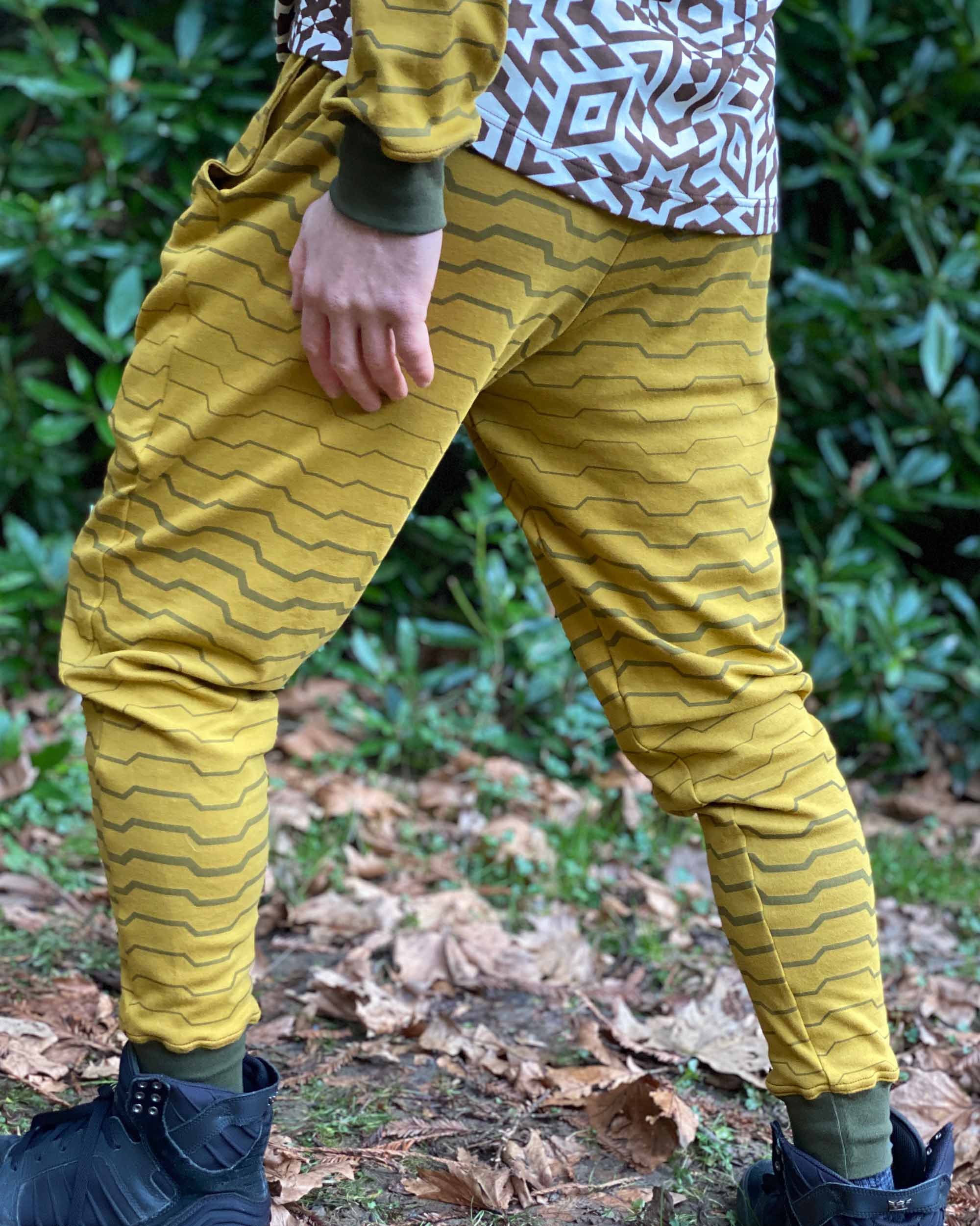 Organic cotton unisex joggers, yellow fabric with brown geometric print, back left side view on male model in nature.