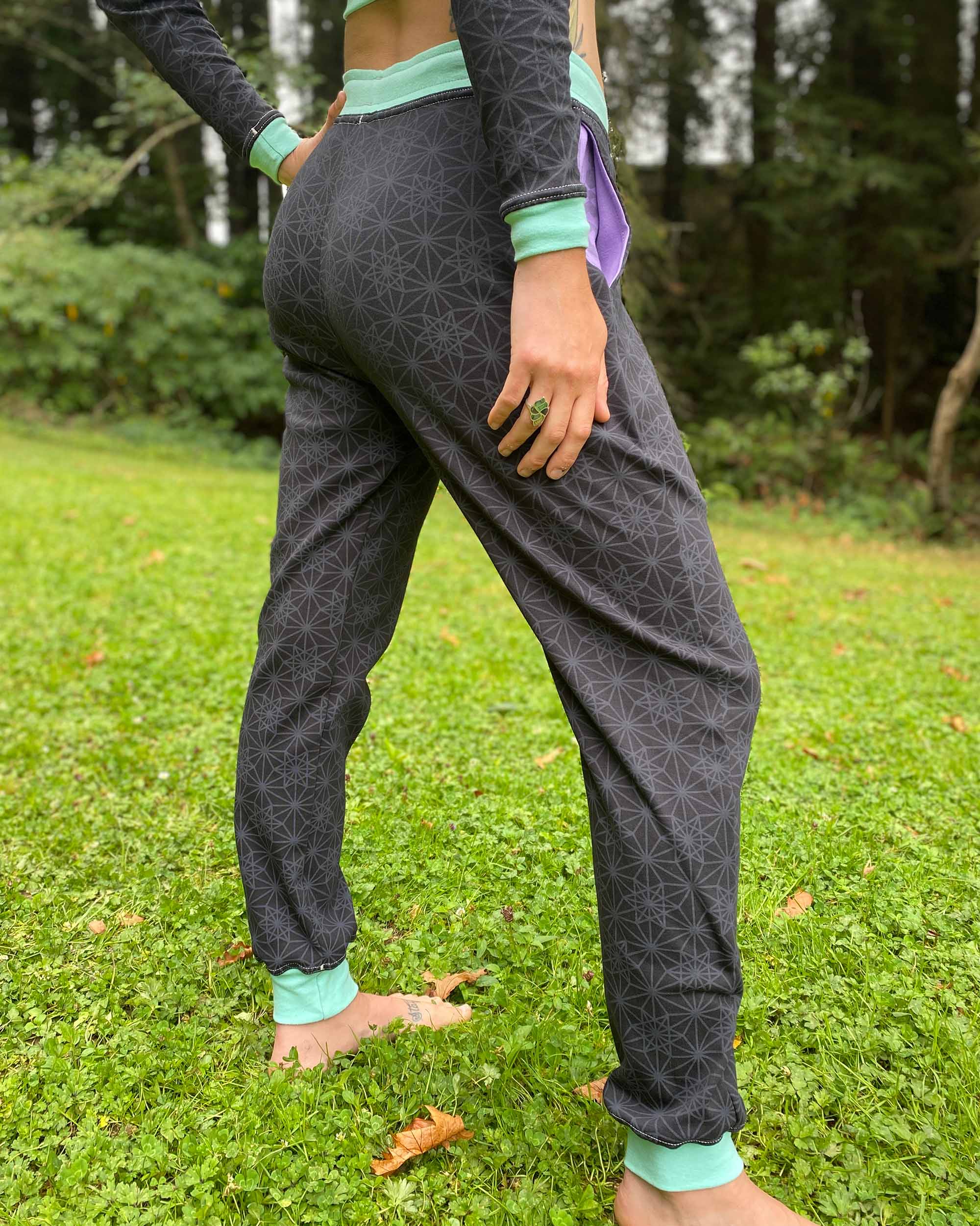 Organic cotton unisex joggers, black fabric with geometric print and purple accents, back view on female.