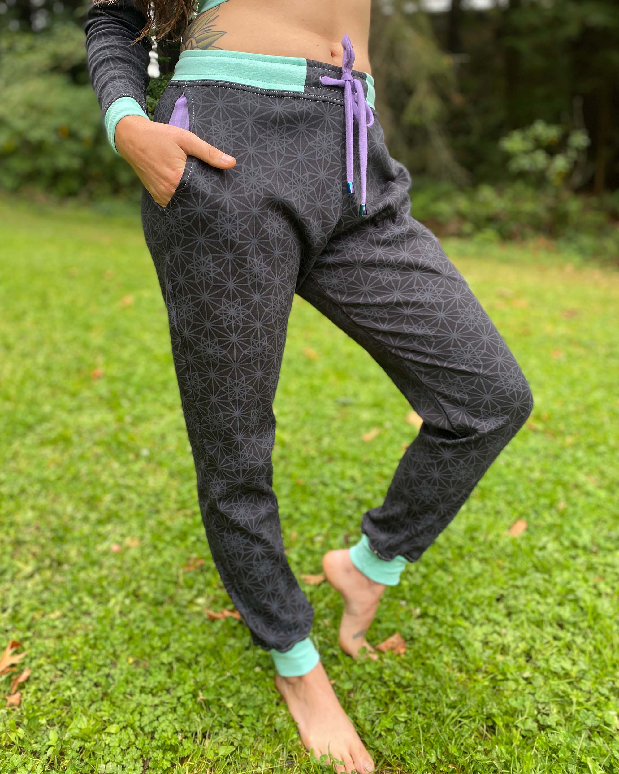 Organic cotton unisex joggers, black fabric with geometric print and purple accents, right side view on female.