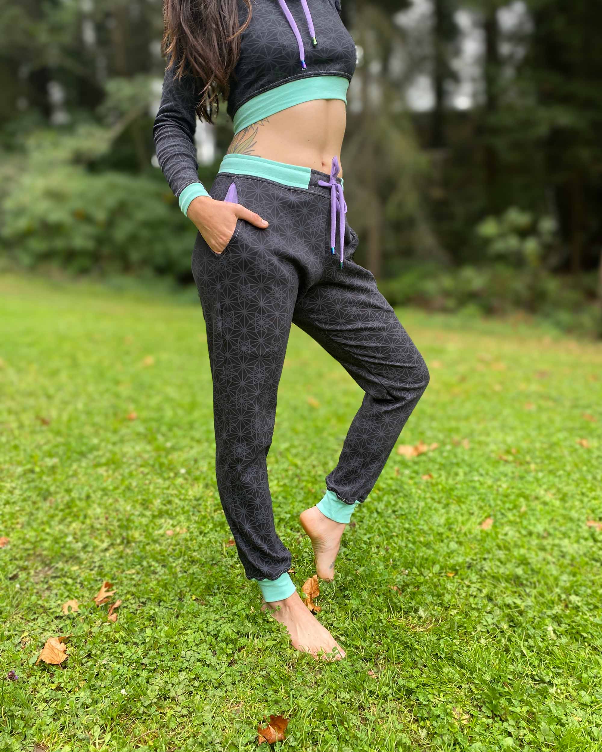 Organic cotton unisex joggers, black fabric with geometric print and purple accents, full body front view on female.