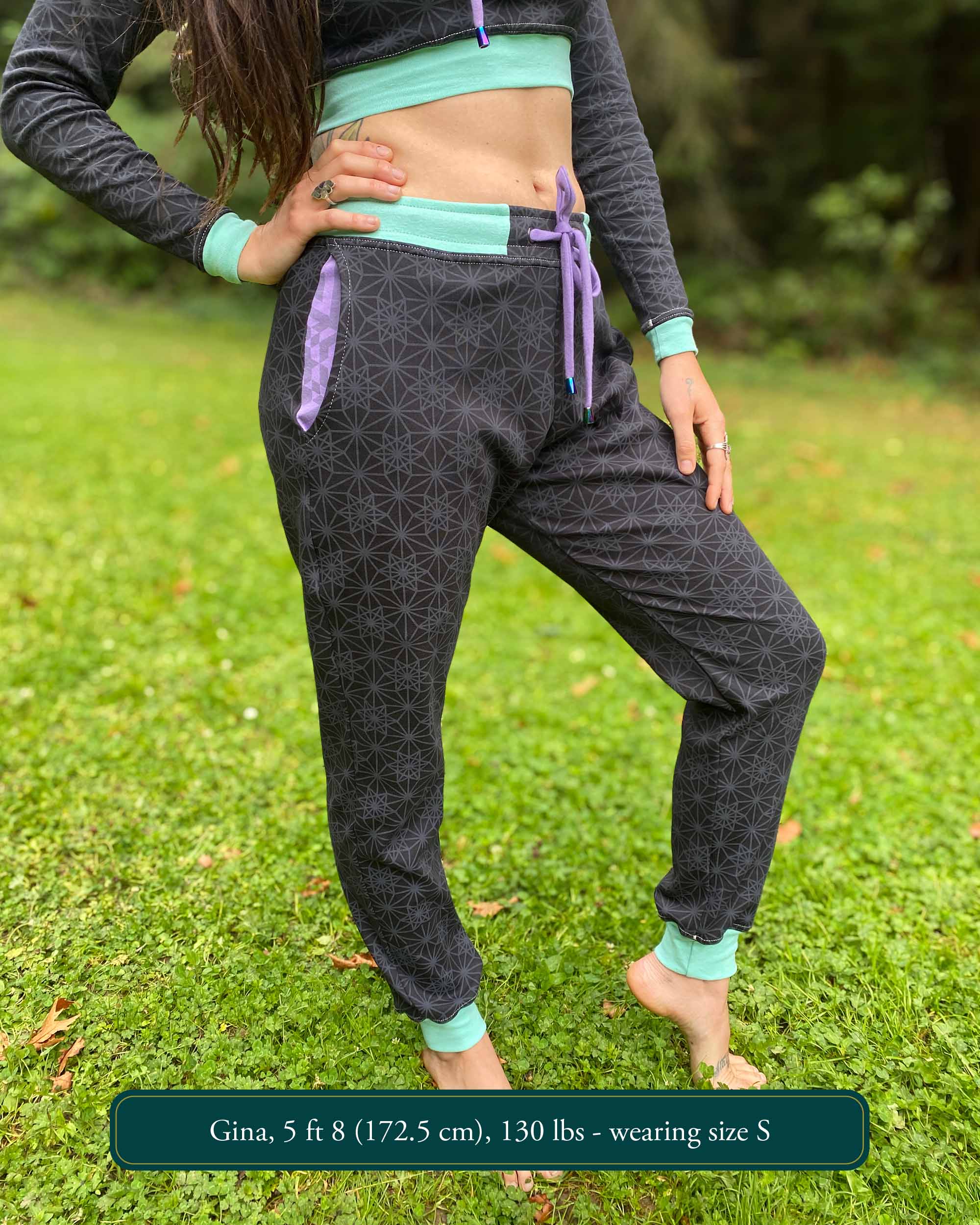 Organic cotton unisex joggers, black fabric with geometric print and purple accents, front view on female.