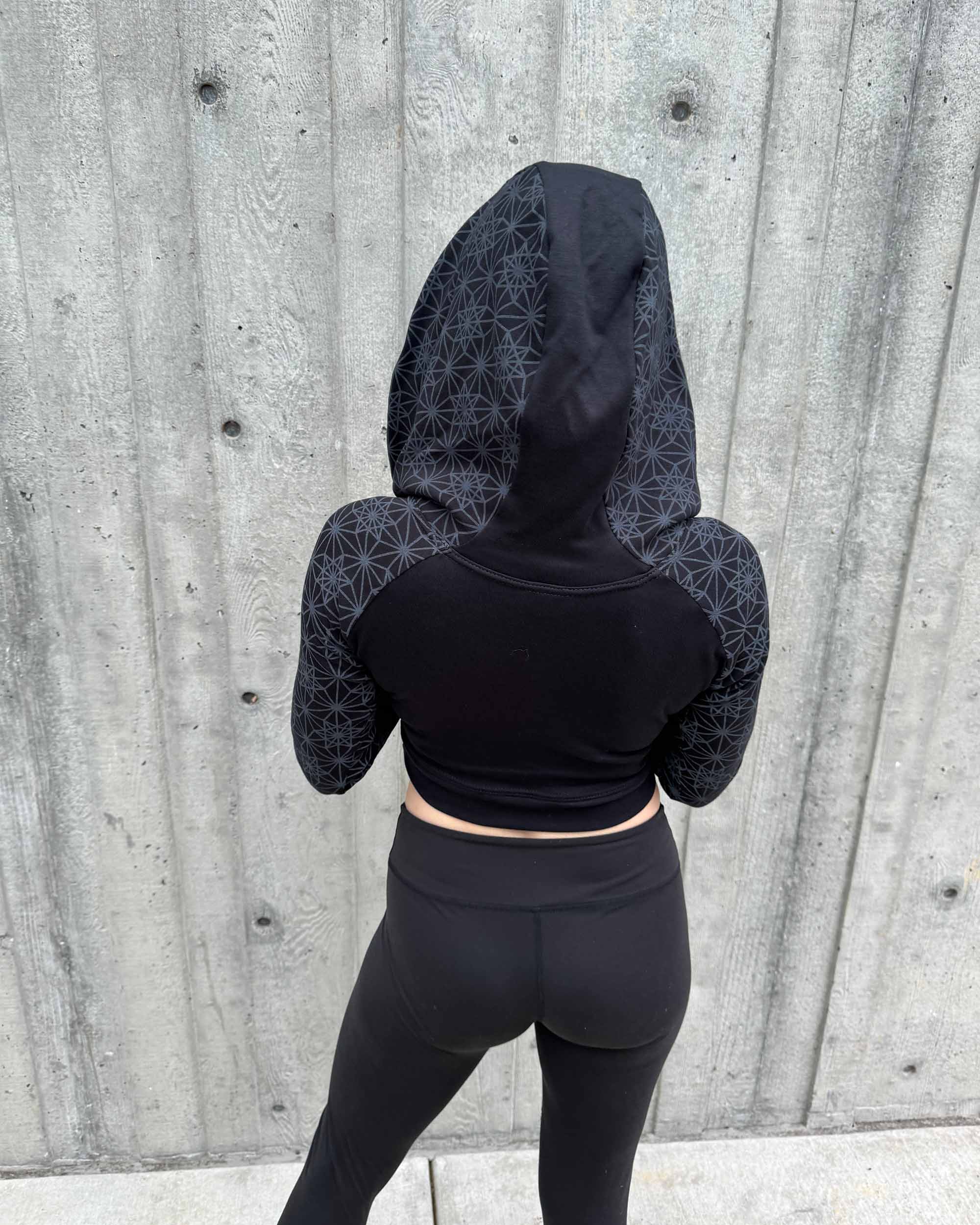 Fitted crop hoodie with cowl hood, black fabric with geometric print, back side view.