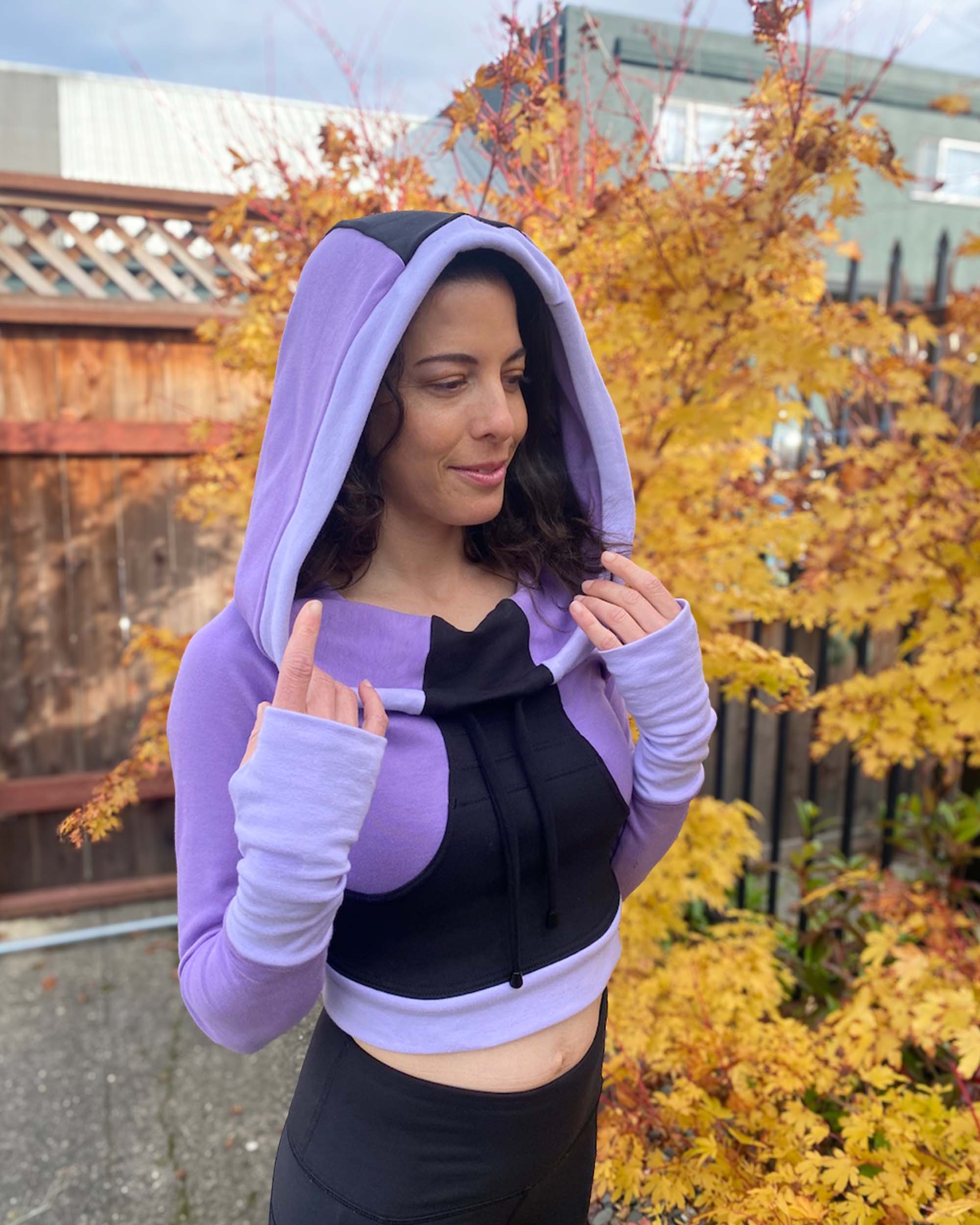 Fitted crop hoodie with cowl hood, black fabric with lavender accent, right side view on model.