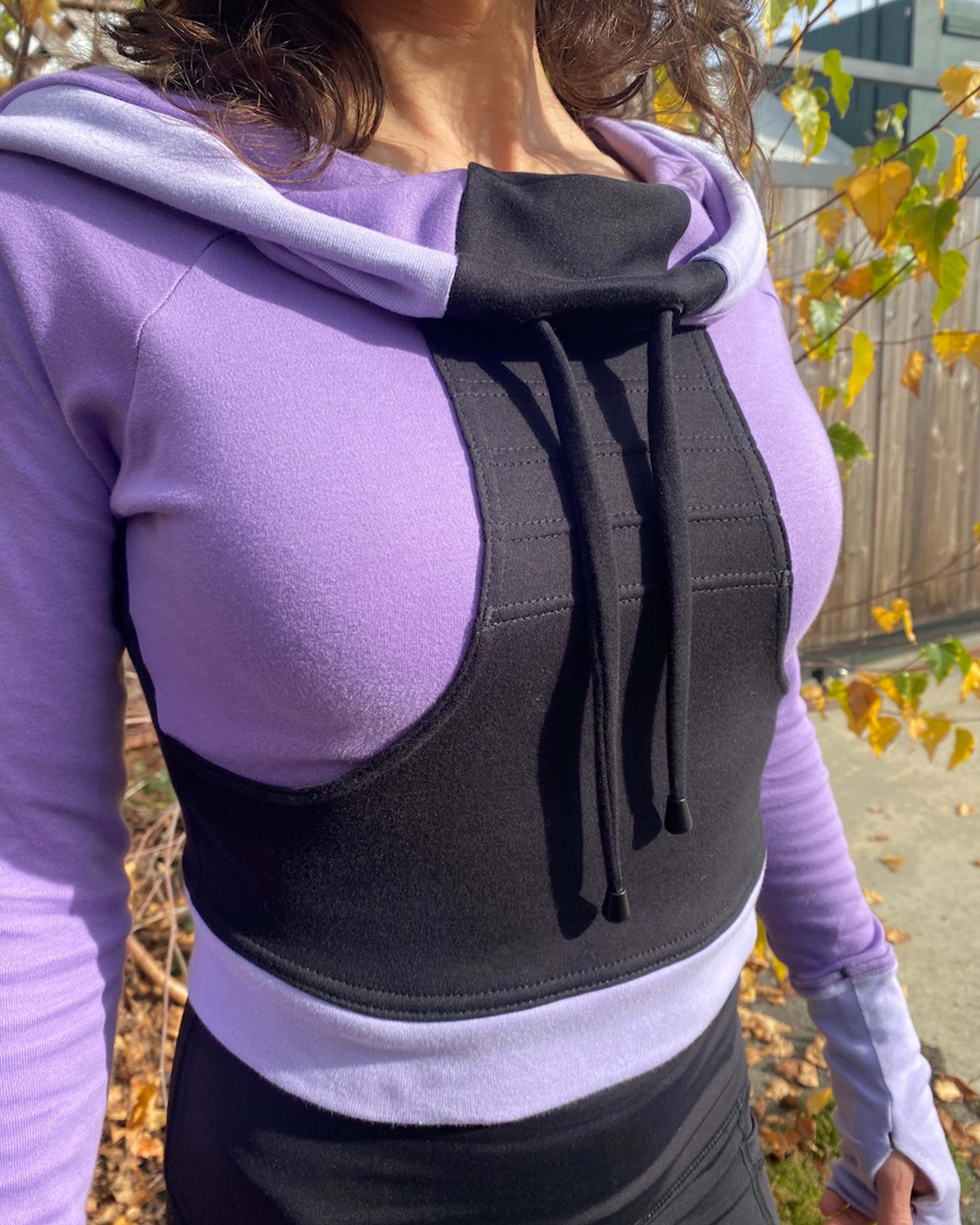 Fitted crop hoodie with cowl hood, black fabric with lavender accent, detail view of stitching.