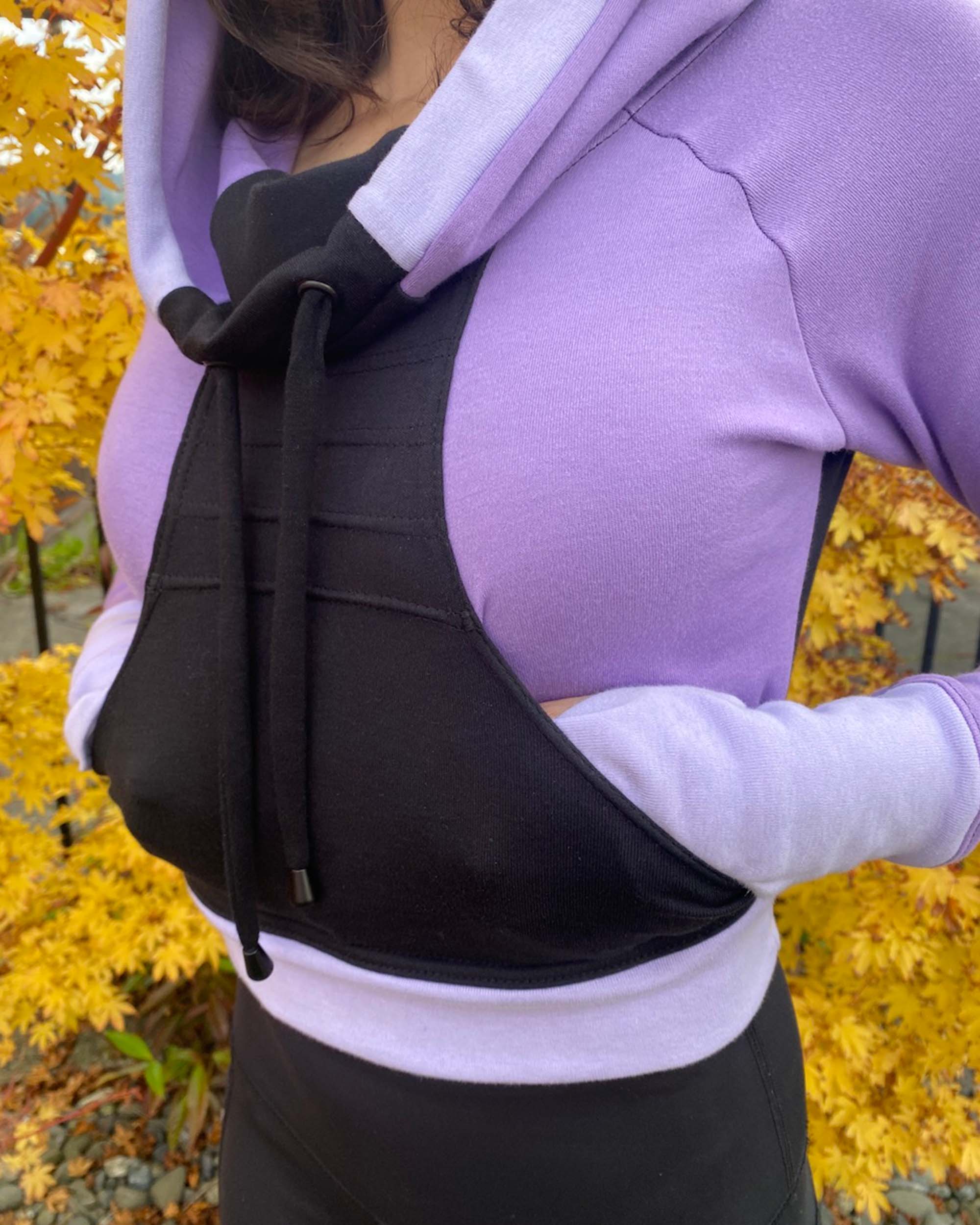 Fitted crop hoodie with cowl hood, black fabric with lavender accent, detail view of pocket.