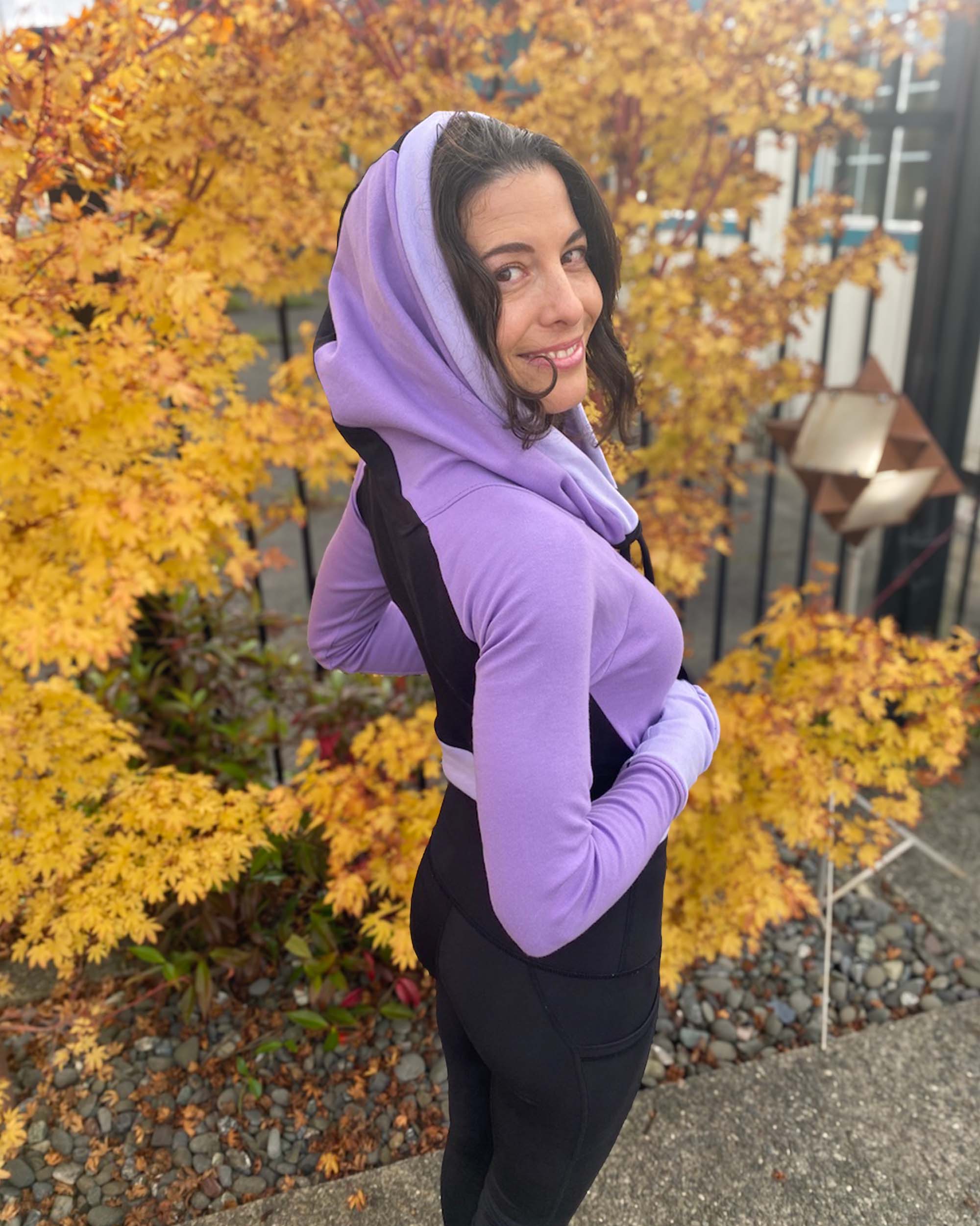 Fitted crop hoodie with cowl hood, black fabric with lavender accent, back side view on model.