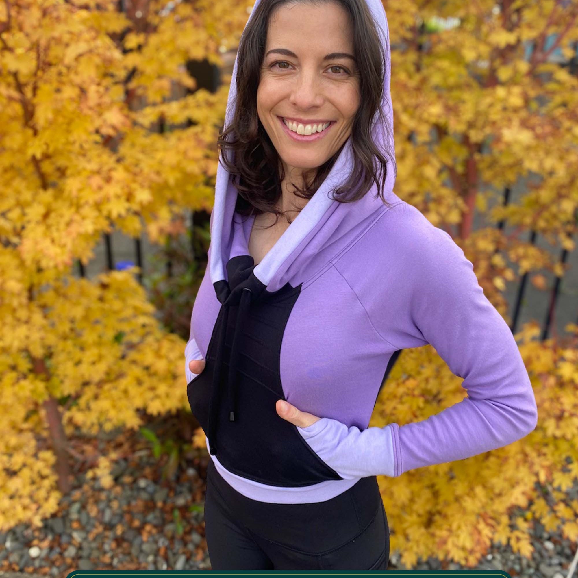 Fitted crop hoodie with cowl hood, black fabric with lavender accent, left side view on model.