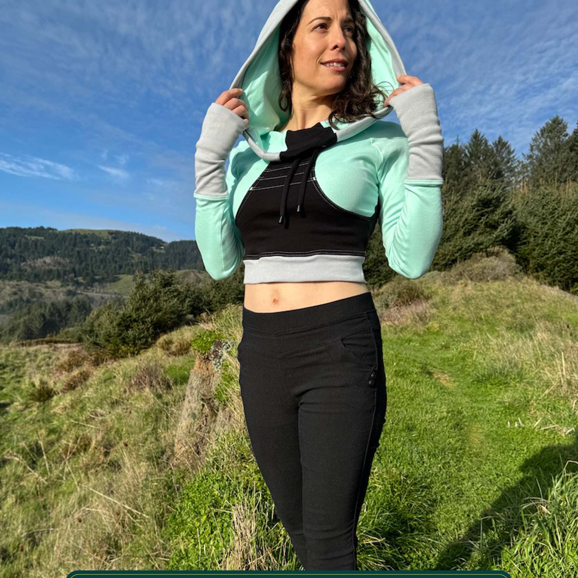 Fitted crop hoodie with cowl hood, mint fabric with black accent, worn by model in the mountains.