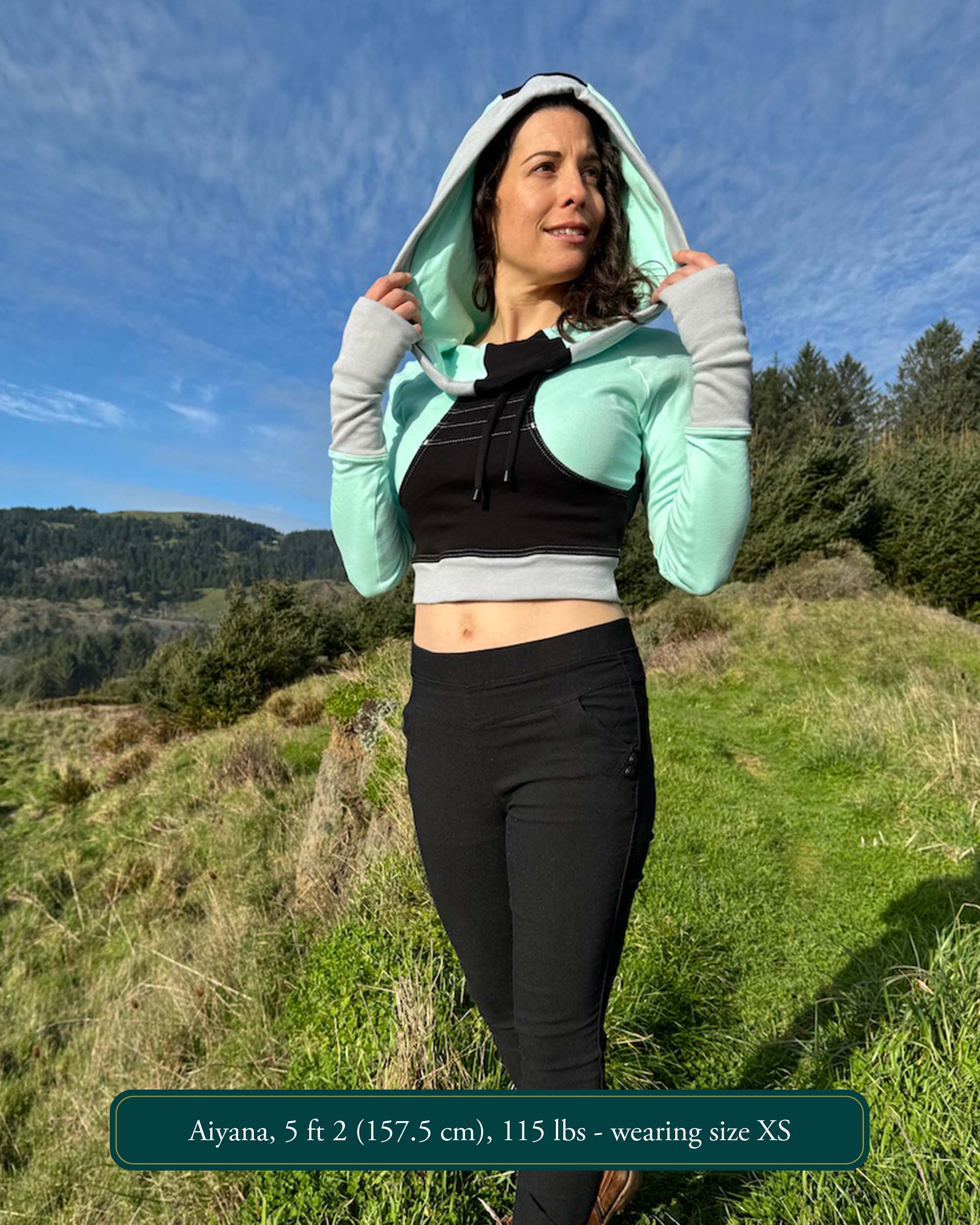 Fitted crop hoodie with cowl hood, mint fabric with black accent, worn by model in the mountains.