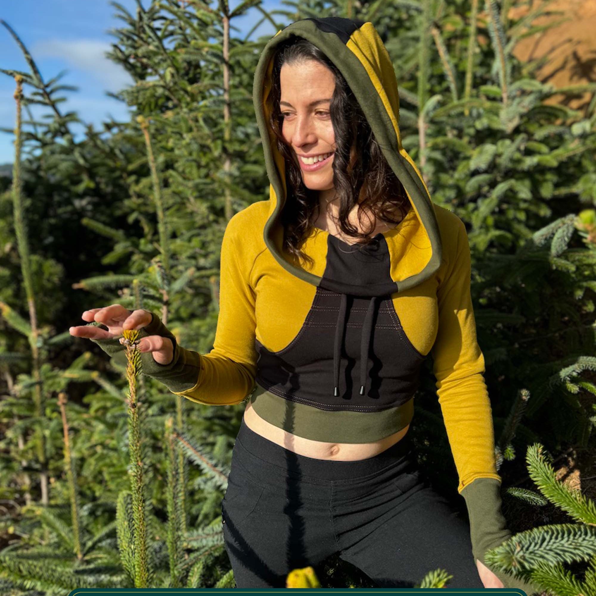 Fitted crop hoodie with cowl hood, yellow fabric with black and green accents, worn by female model.