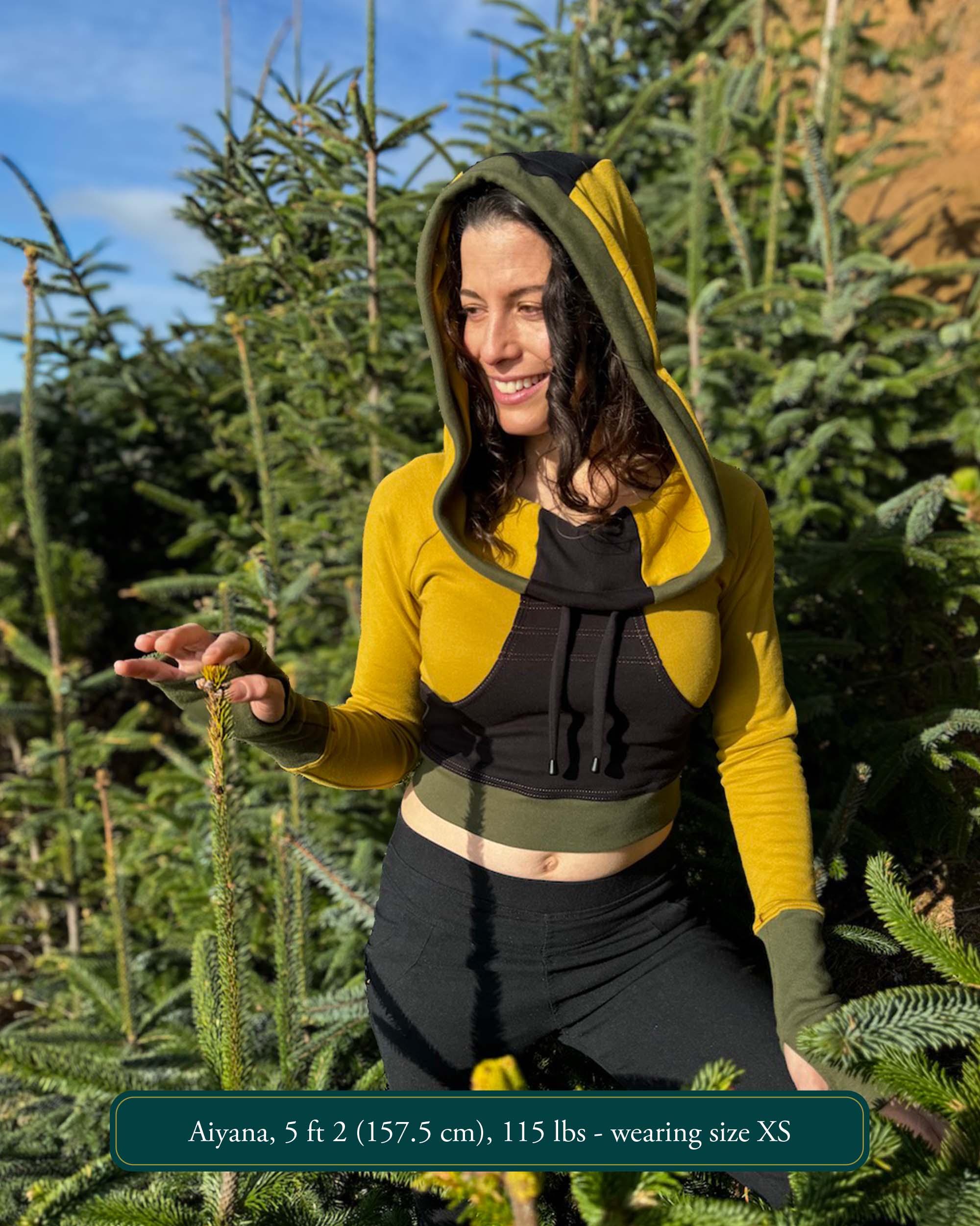 Fitted crop hoodie with cowl hood, yellow fabric with black and green accents, worn by female model.