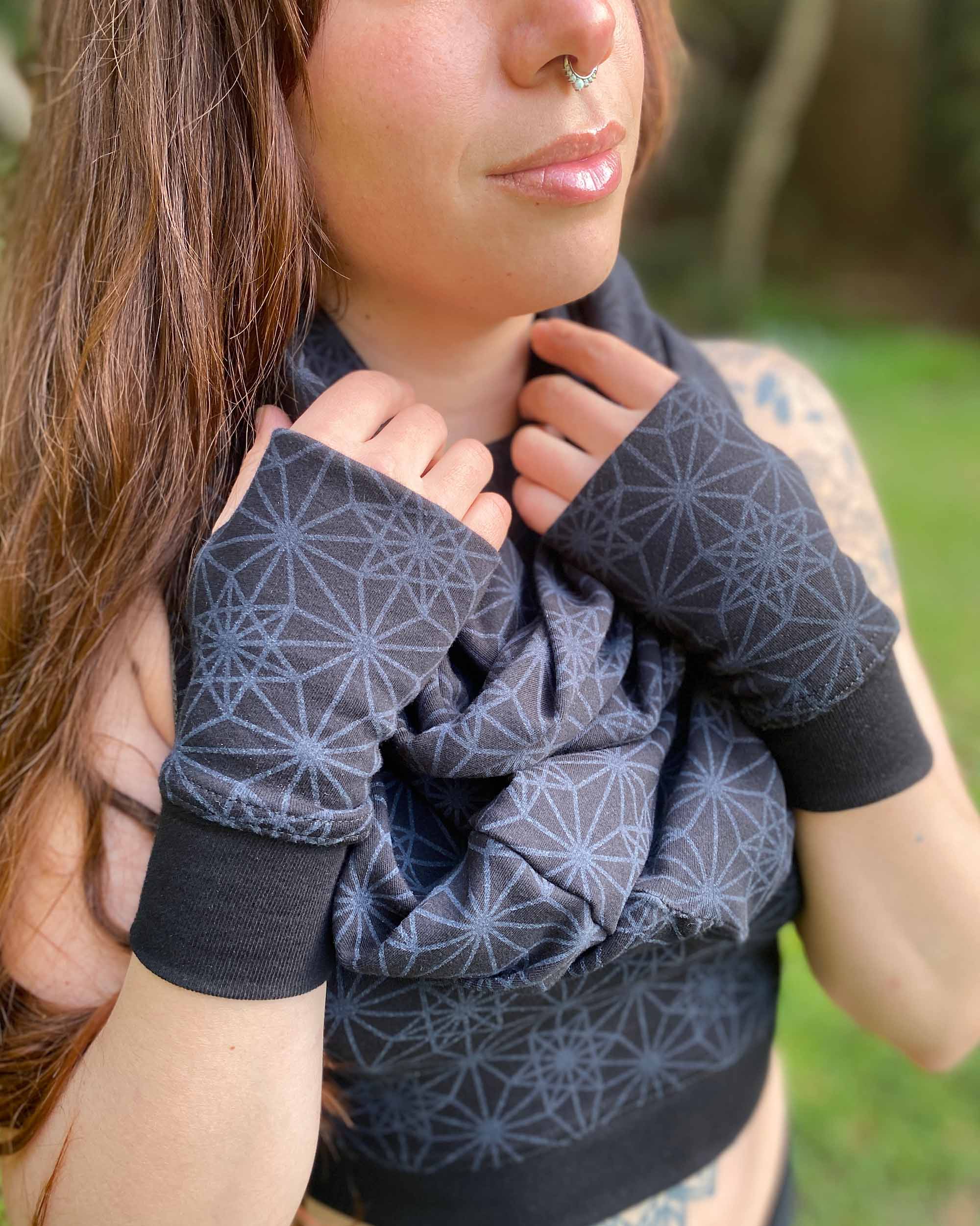 Female model wearing matching set of crop top, infinity scarf and fingerless gloves, black organic cotton fabric with geometric print, detail view of scarf.