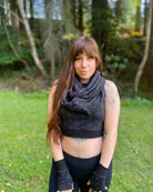 Female model wearing matching set of crop top, infinity scarf and fingerless gloves, black organic cotton fabric with geometric print, front view in nature.