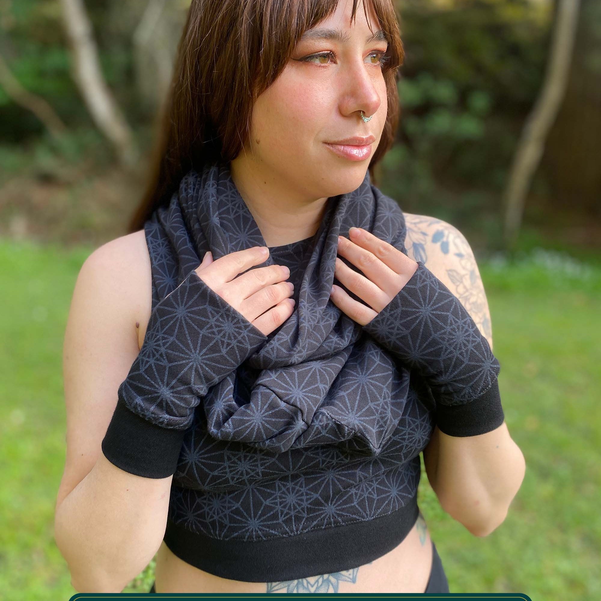 Female model wearing matching set of crop top, infinity scarf and fingerless gloves, black fabric with geometric print, front view.
