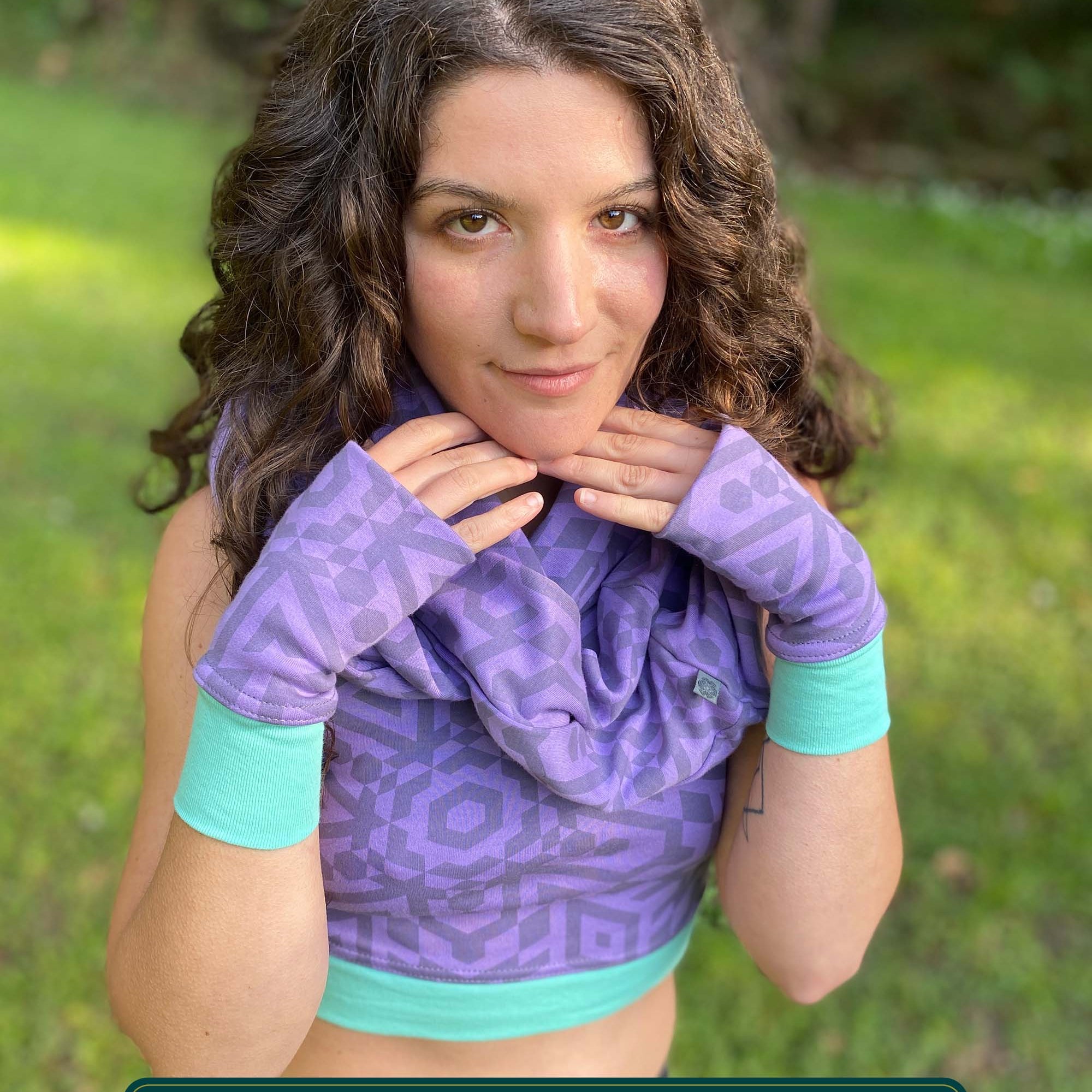 Female model wearing matching set of crop top, infinity scarf and fingerless gloves, lavender organic cotton fabric with geometric print, front view.