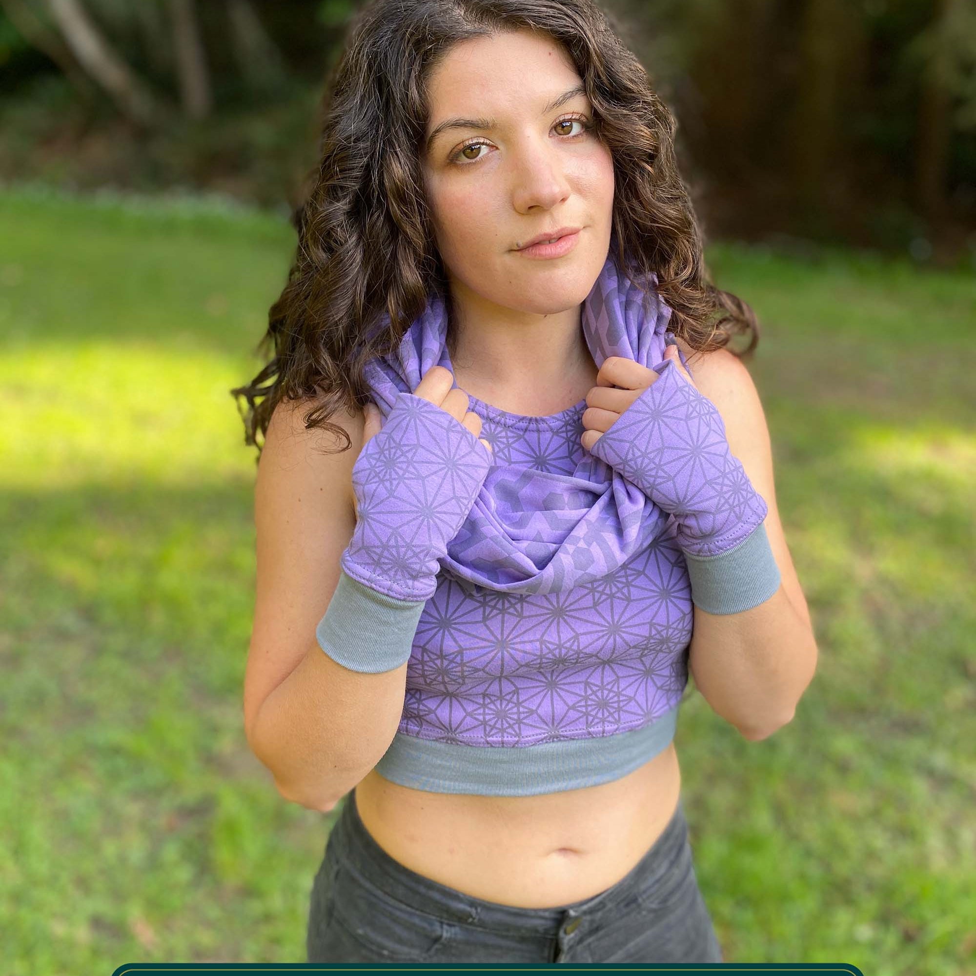 Female model wearing matching set of crop top, infinity scarf and fingerless gloves, purple organic cotton fabric with geometric print, front view.