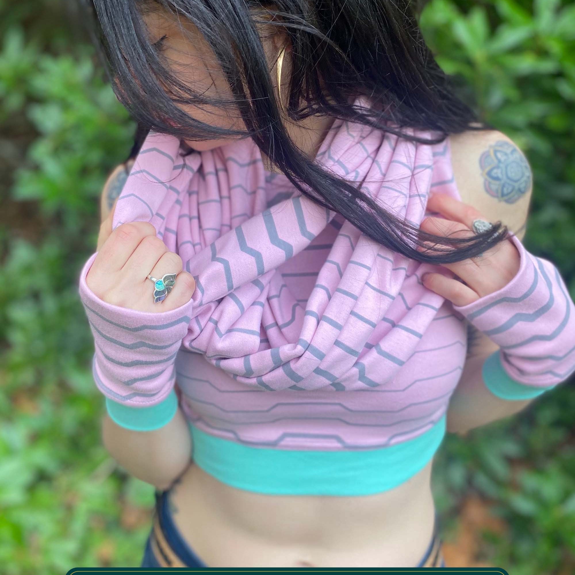 Female model wearing matching set of crop top, infinity scarf and fingerless gloves, pink organic cotton fabric with geometric stripes, front view.
