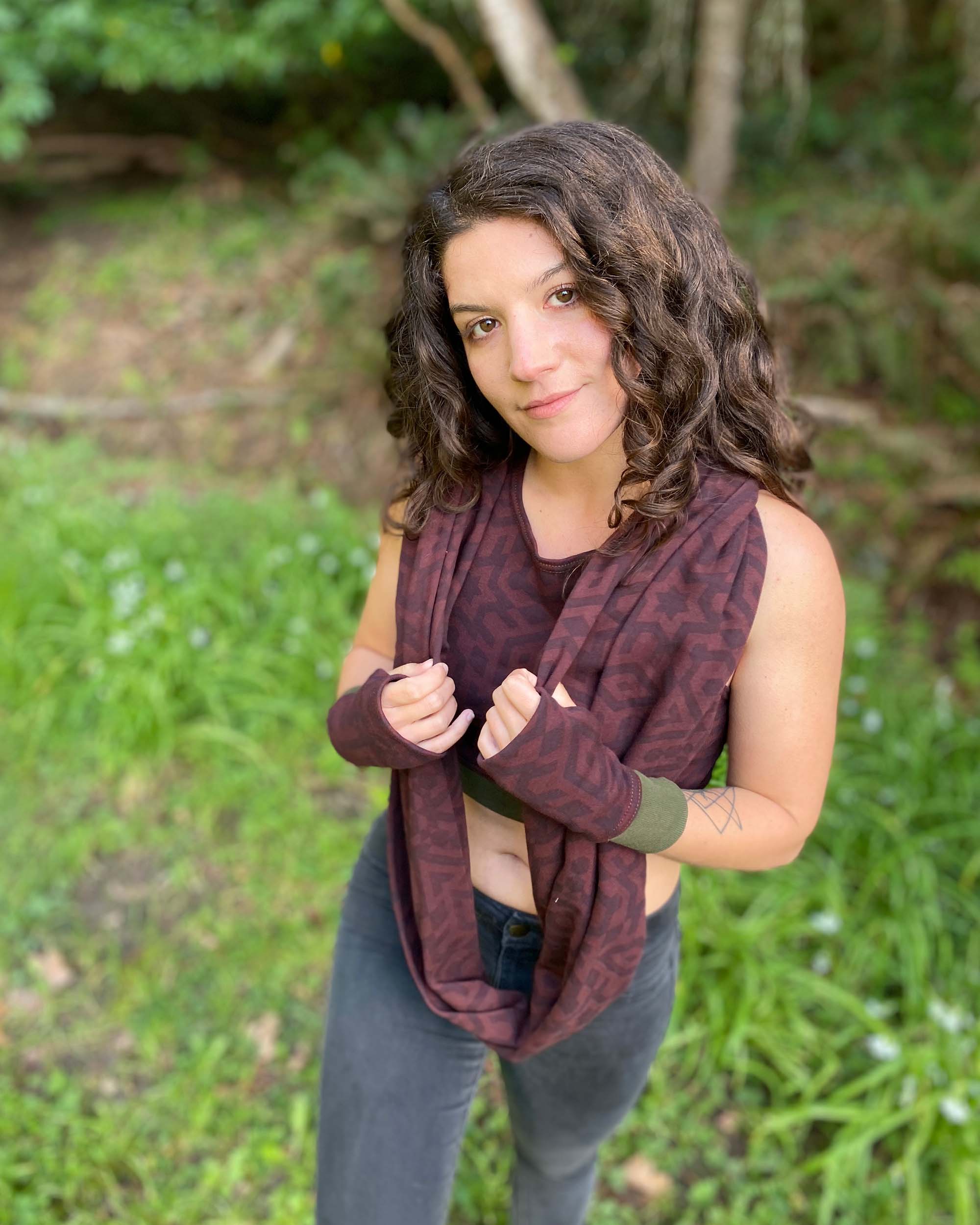 Female model wearing matching set of crop top, infinity scarf and fingerless gloves, brown organic cotton fabric with geometric print, front right side view.