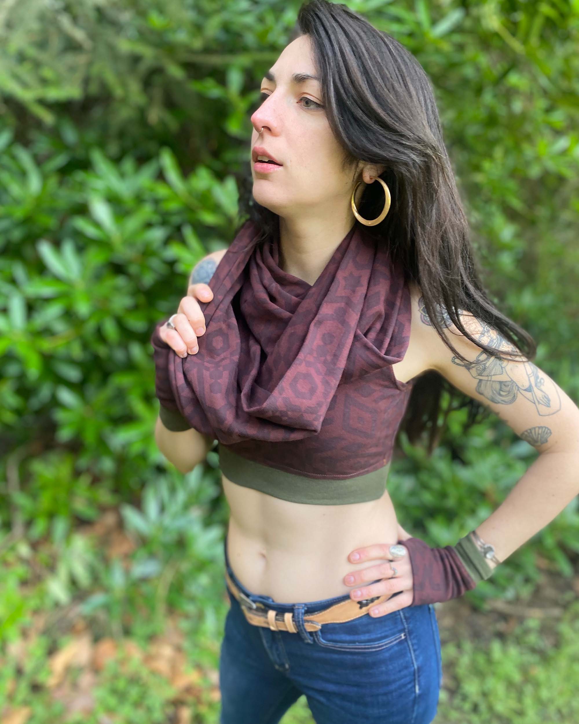 Female model wearing matching set of crop top, infinity scarf and fingerless gloves, brown organic cotton fabric with geometric print, front side view.
