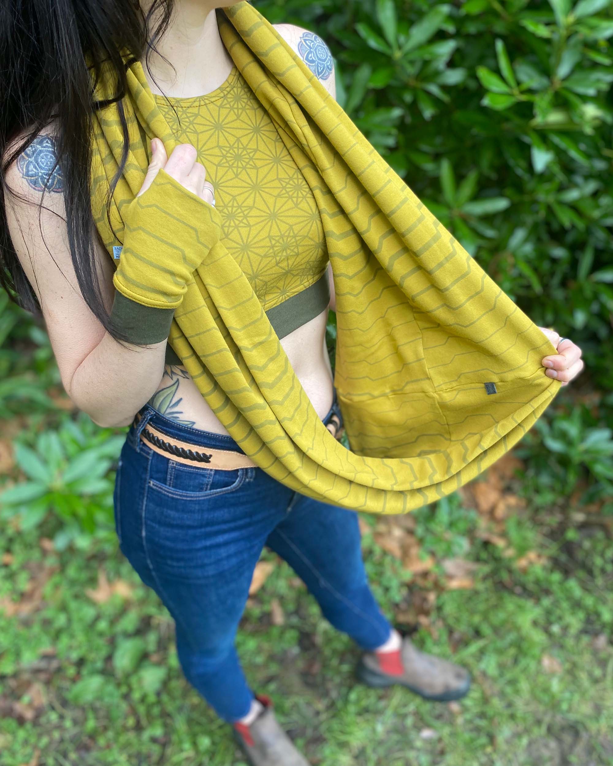 Female model wearing matching set of crop top, infinity scarf and fingerless gloves, yellow organic cotton fabric with geometric stripes, detail view of scarf.