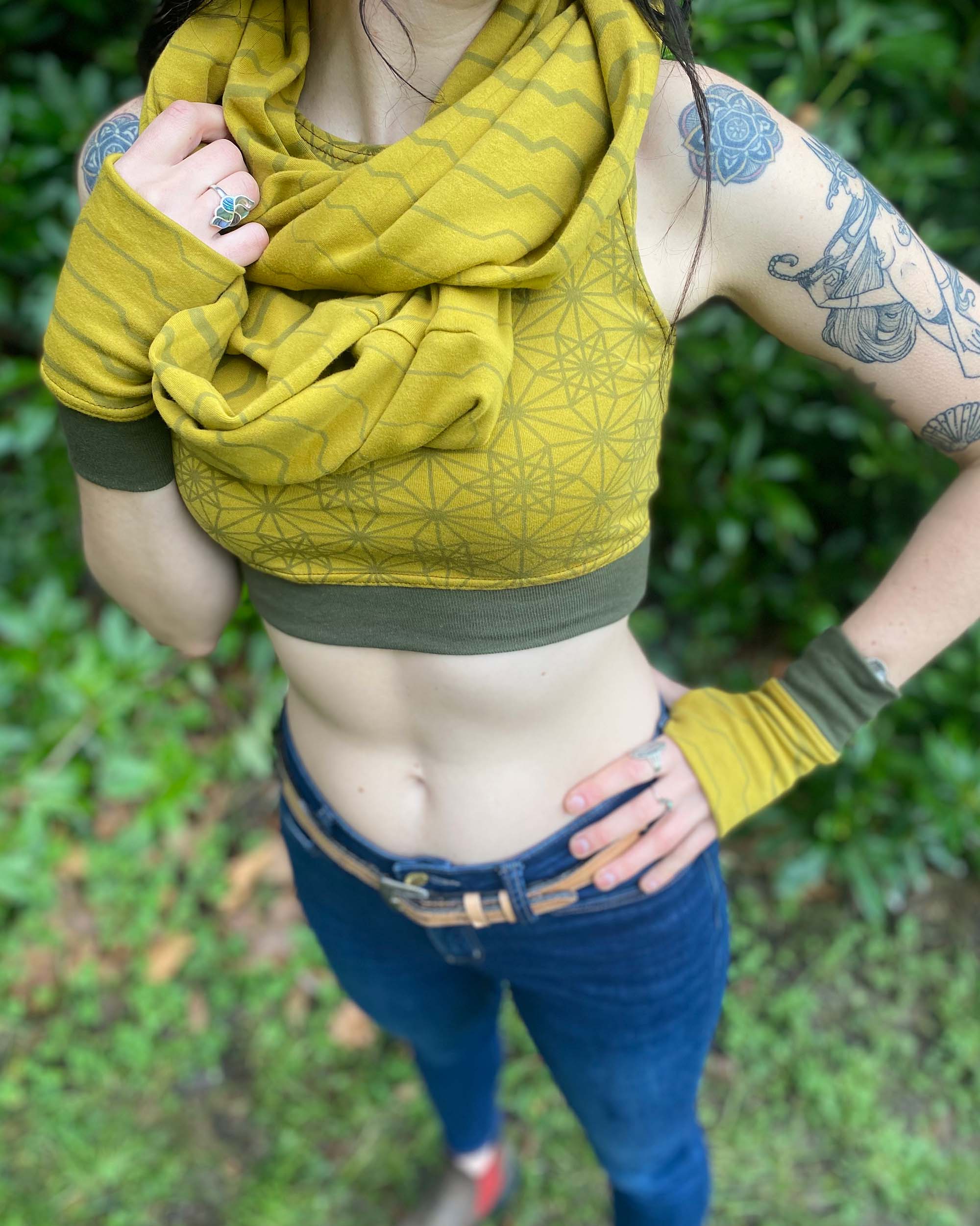 Female model wearing matching set of crop top, infinity scarf and fingerless gloves, yellow organic cotton fabric with geometric stripes, close up view.