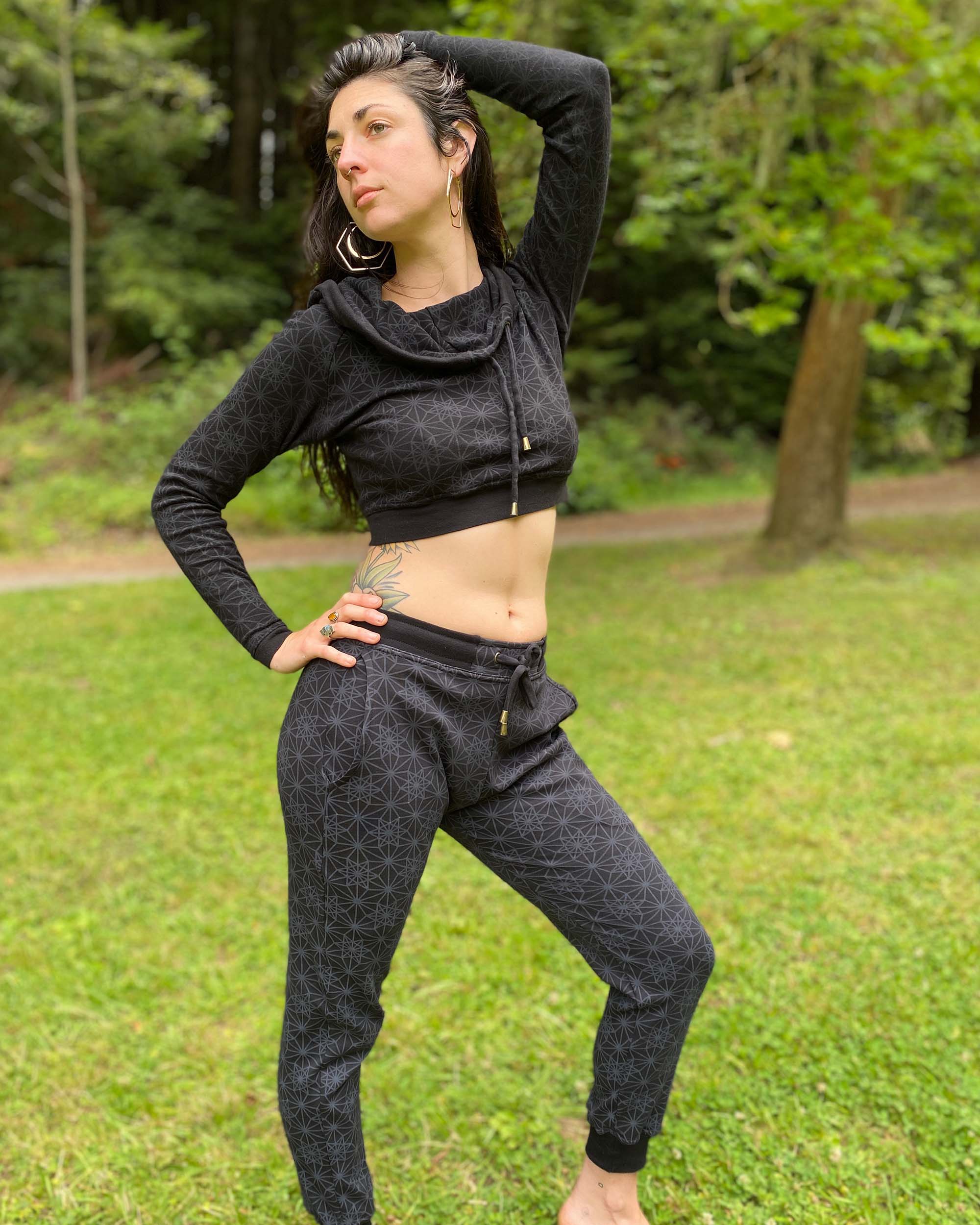 Matching two piece set, joggers and crop hoodie, black fabric with geometric print, front view on female model.