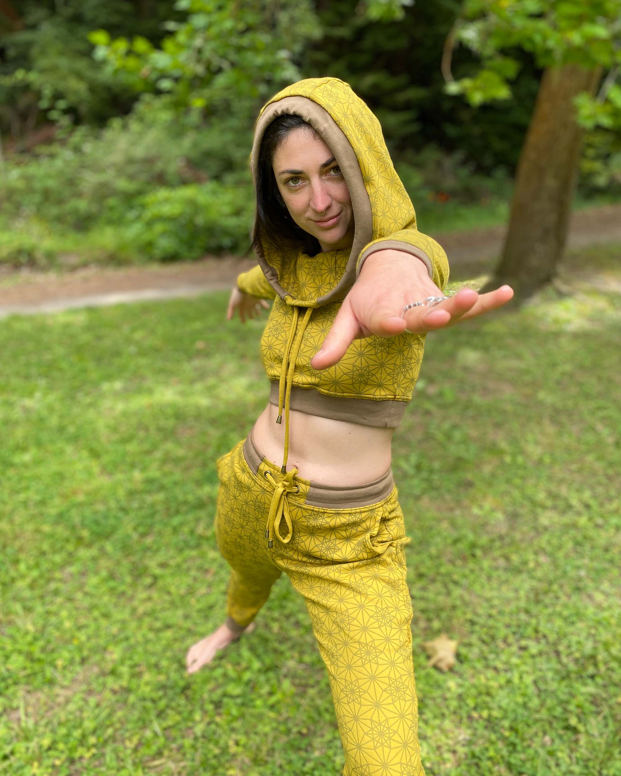 Women's matching two piece outfit, joggers and crop hoodie, yellow fabric with geometric print, view of model in yoga pose.