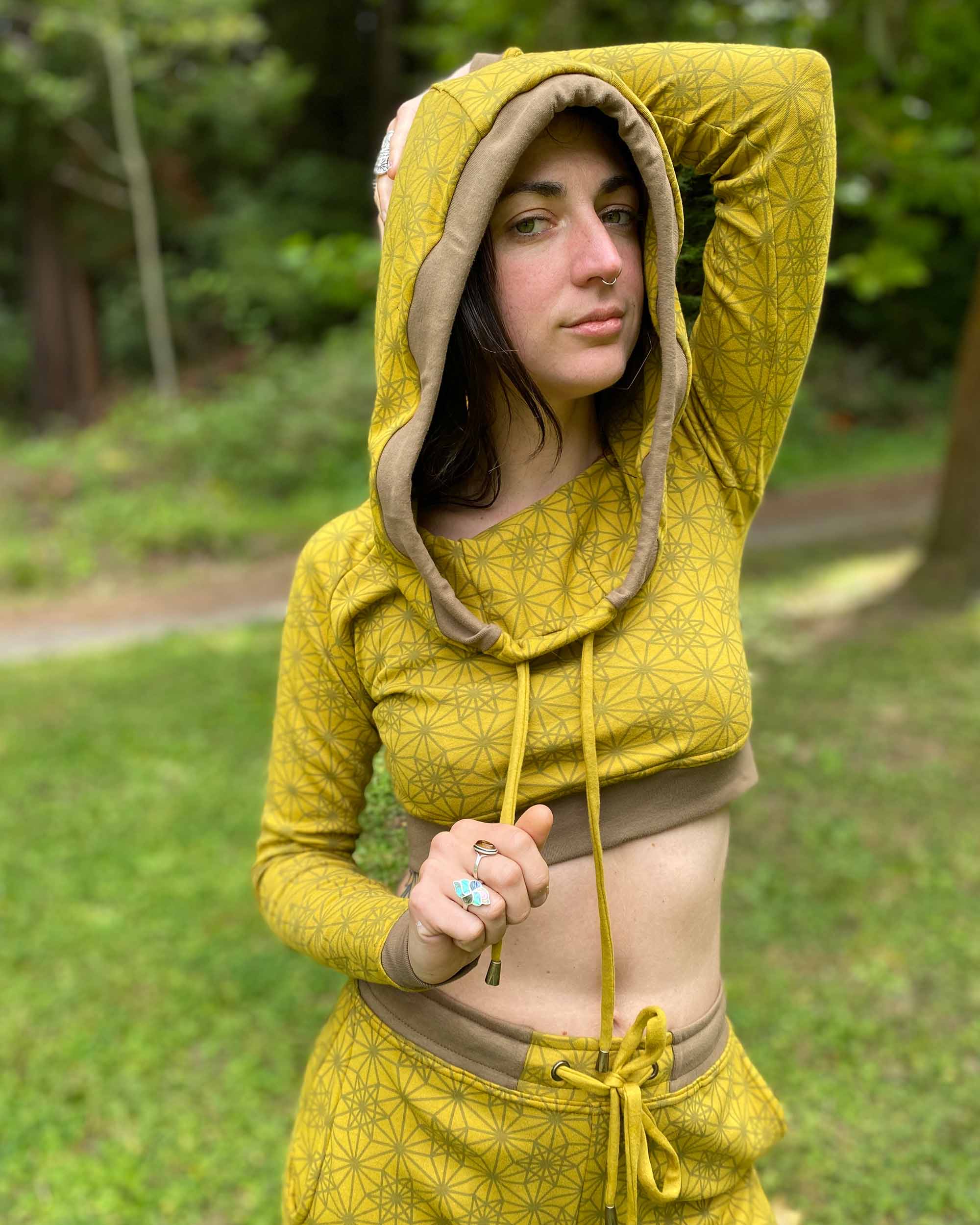 Women's matching two piece outfit, joggers and crop hoodie, yellow fabric with geometric print, close up view on model.