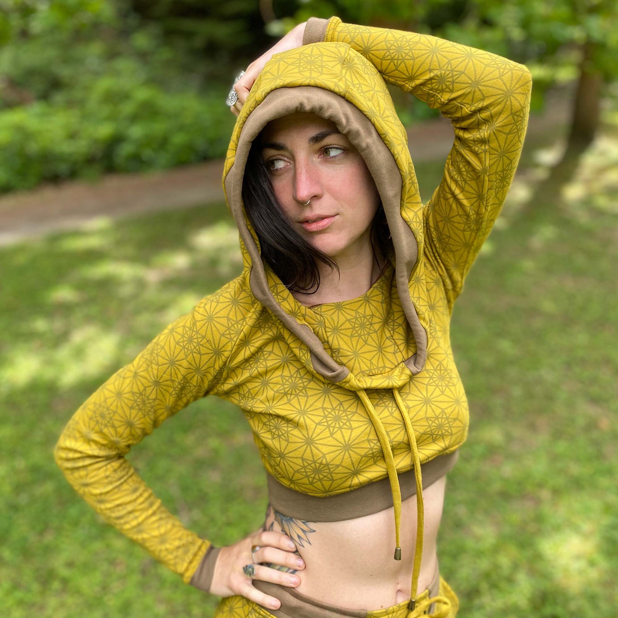 Women's matching two piece outfit, joggers and crop hoodie, yellow fabric with geometric print, worn with hood up on model.