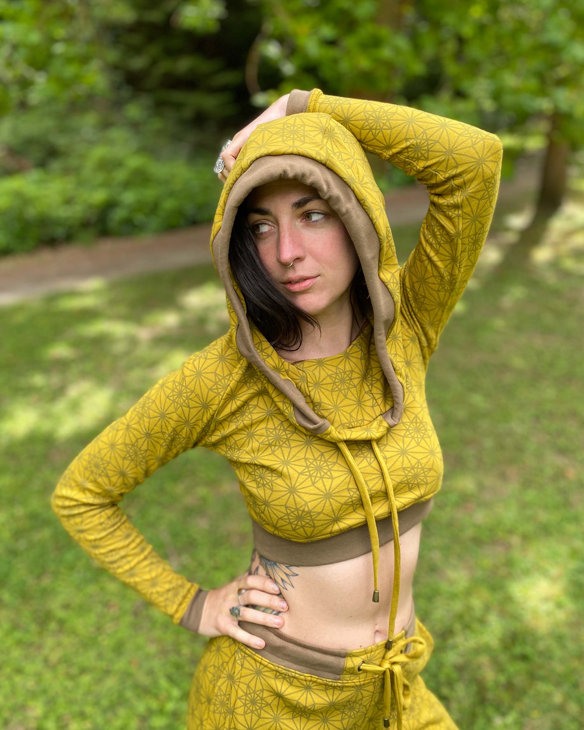 Women's matching two piece outfit, joggers and crop hoodie, yellow fabric with geometric print, worn with hood up on model.