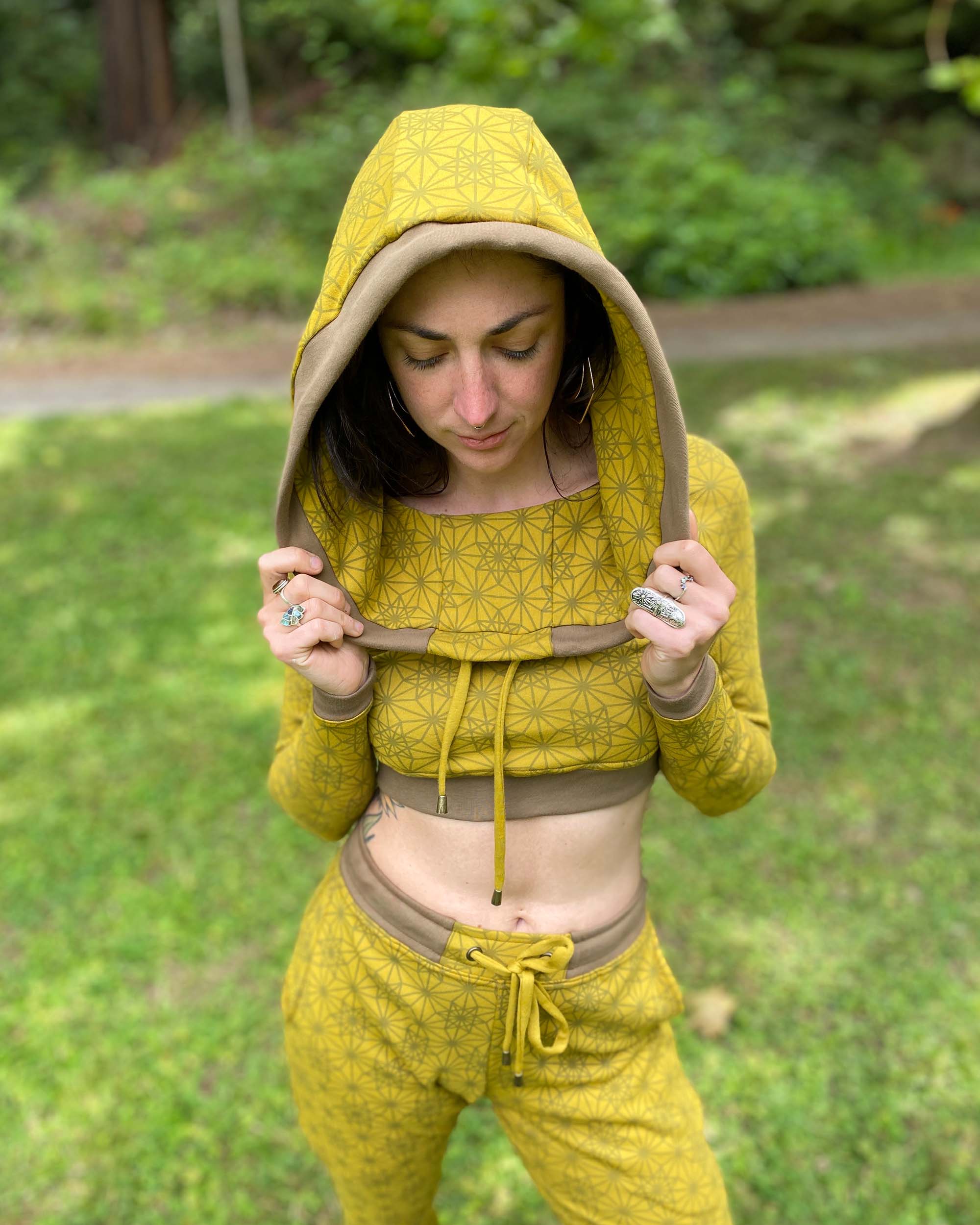 Women's matching two piece outfit, joggers and crop hoodie, yellow fabric with geometric print, front view with hood on.