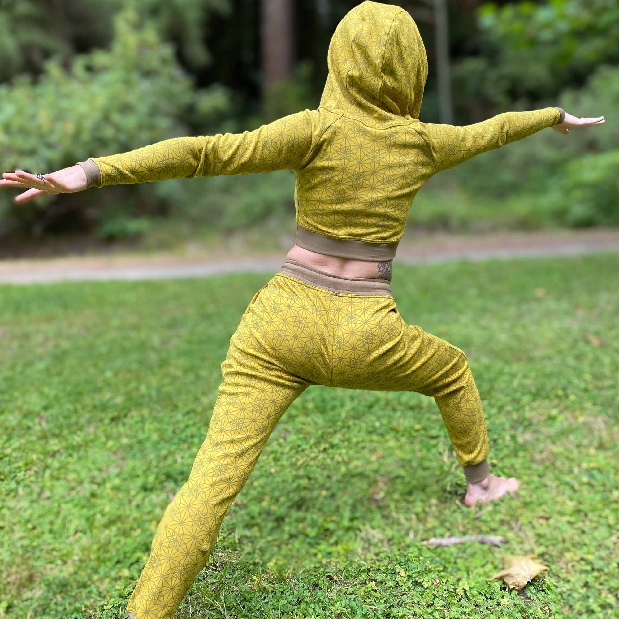 Women's matching two piece outfit, joggers and crop hoodie, yellow fabric with geometric print, model in yoga pose.