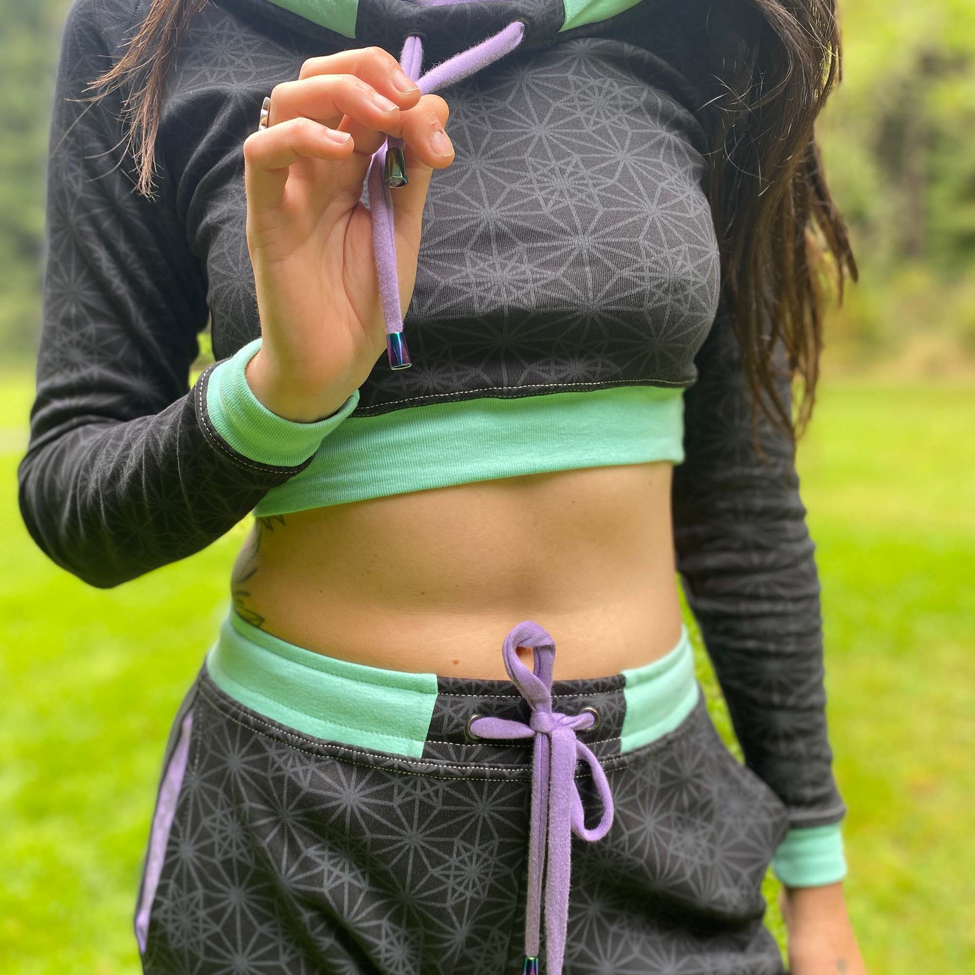 Women's matching two piece set, joggers and crop hoodie, black with lavender geometric accents, close up view of drawcords.