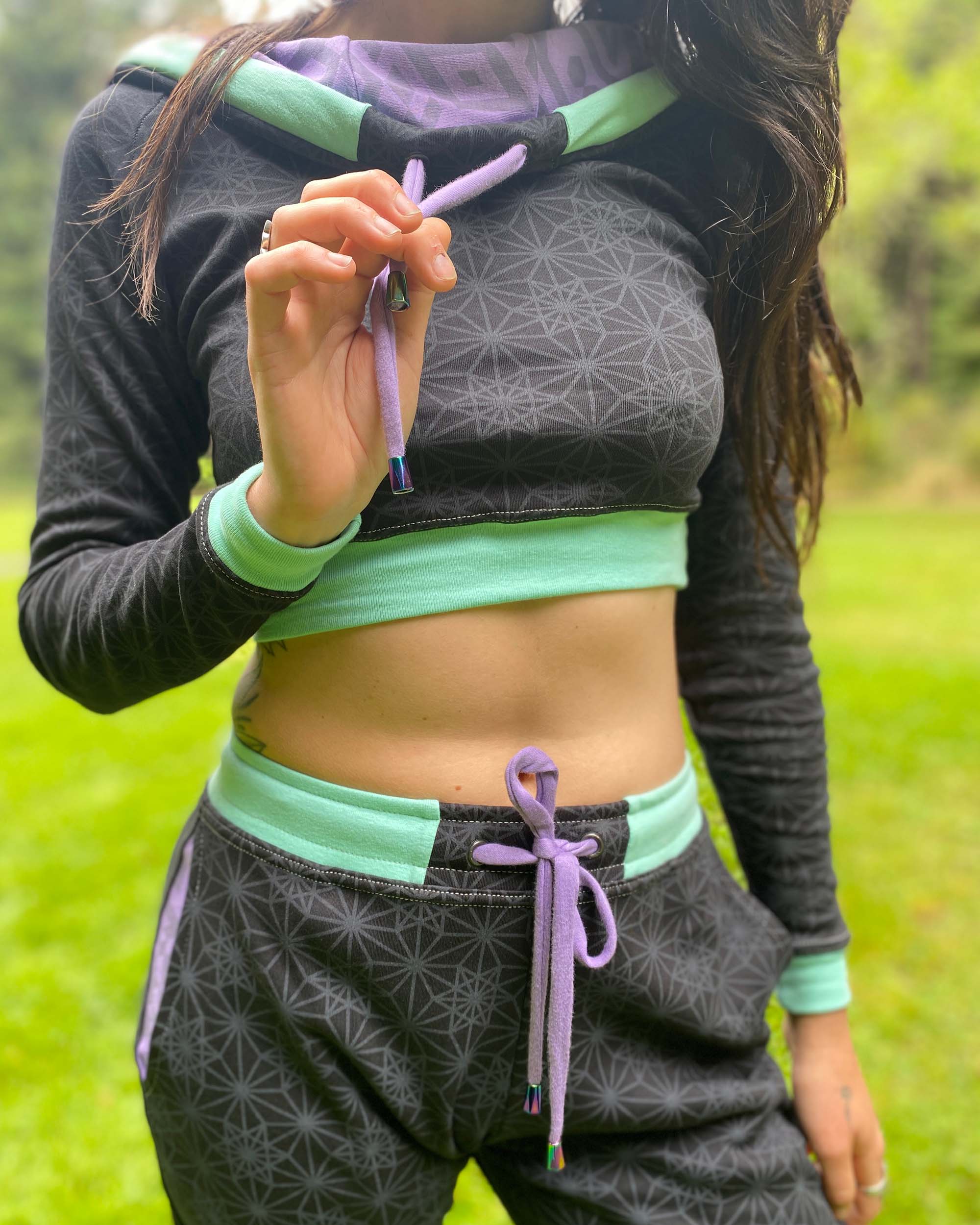 Women's matching two piece set, joggers and crop hoodie, black with lavender geometric accents, close up view of drawcords.