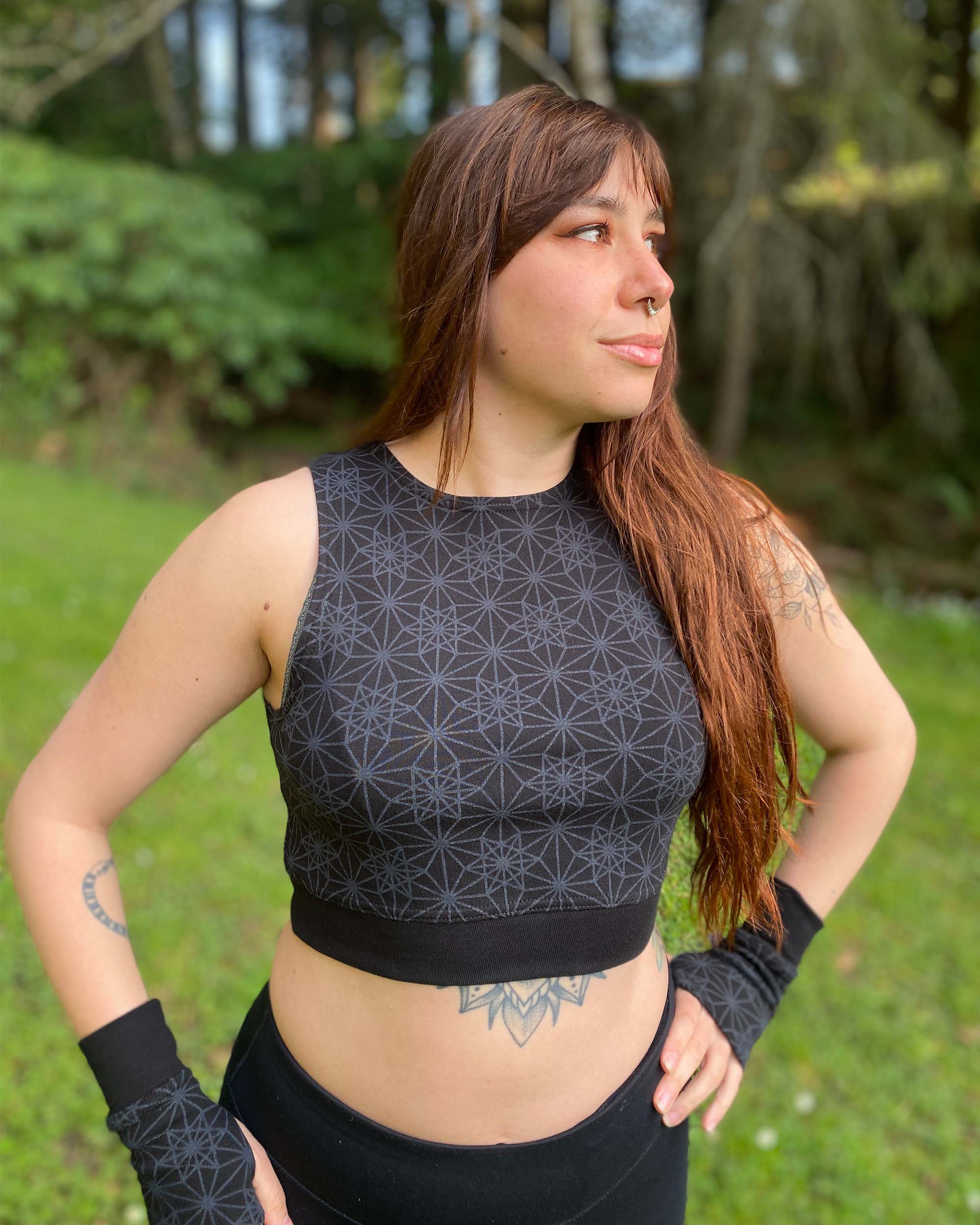 Organic cotton crop top, black fabric with sacred geometry print, front view on female model in nature.