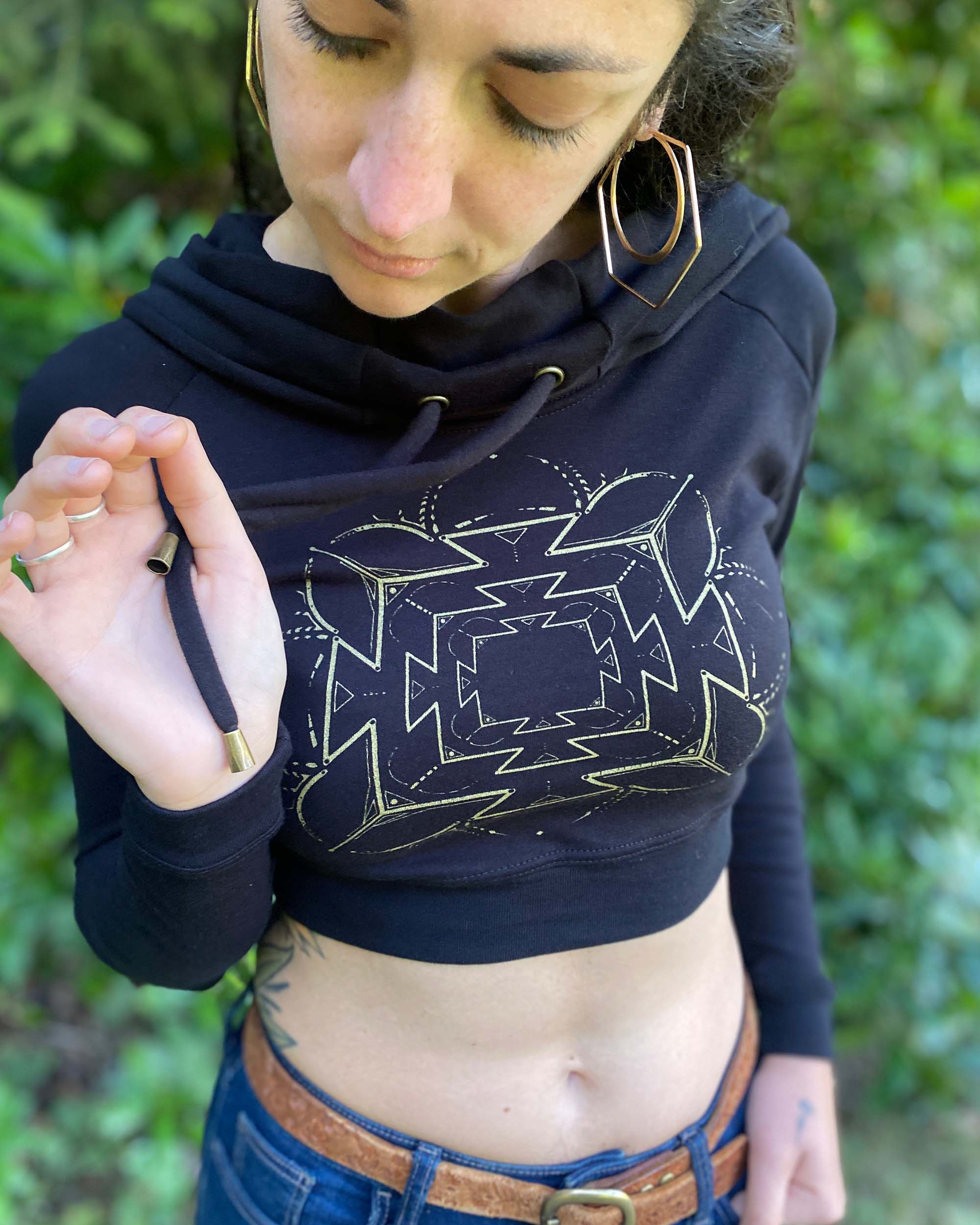 A woman wearing an organic cotton black crop hoodie with a gold print, detail view of drawcord.