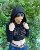 A woman wearing an organic cotton black crop hoodie with a gold print on the front center, front view.