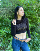 A woman wearing an organic cotton black crop hoodie with a gold print, worn with cowl hood up, front view in nature.