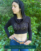 A woman wearing an organic cotton black crop hoodie with a gold print, worn with cowl hood up, front view.