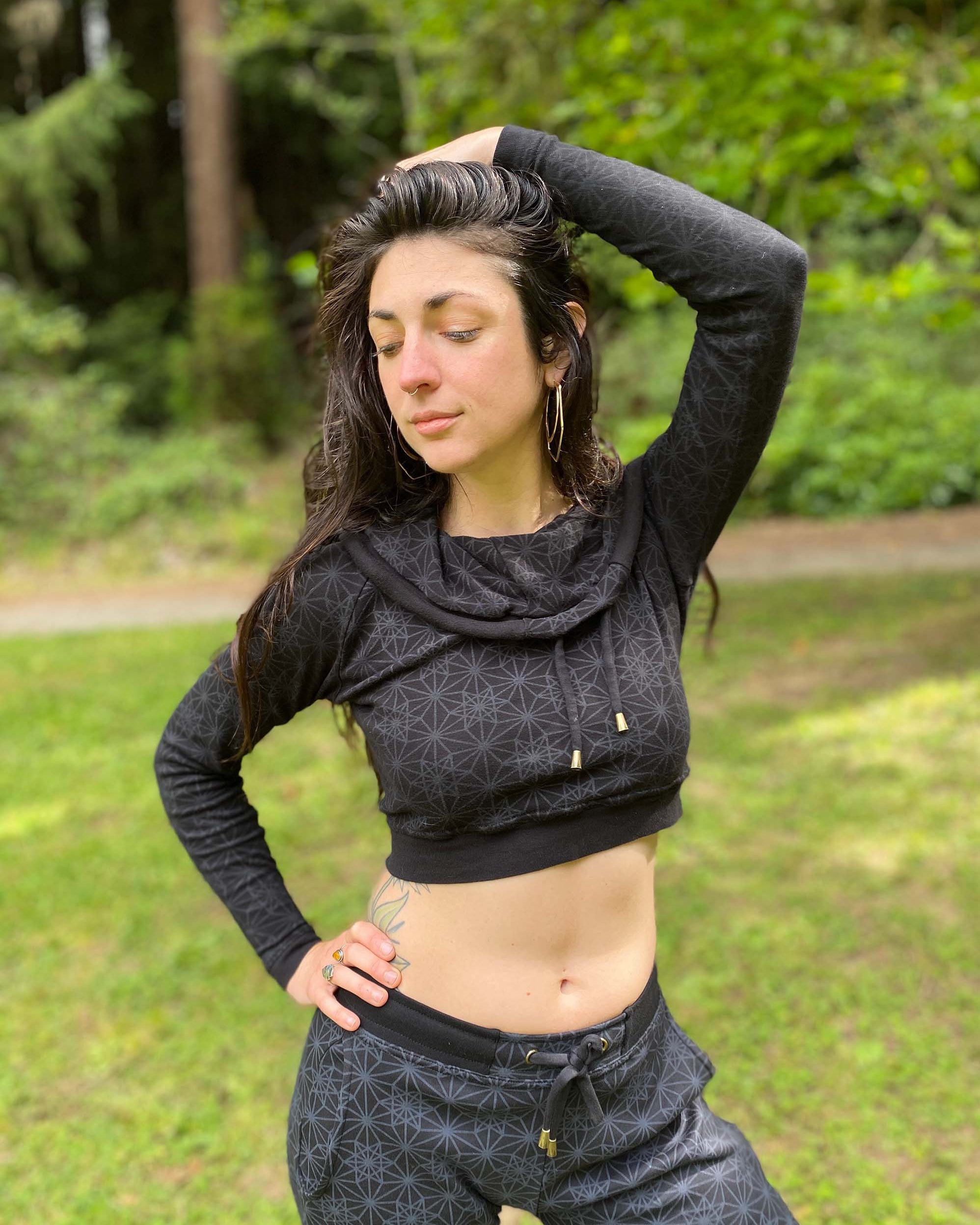 A woman wearing an organic cotton black crop hoodie with geometric print, with matching joggers, side view in a outdoor setting.