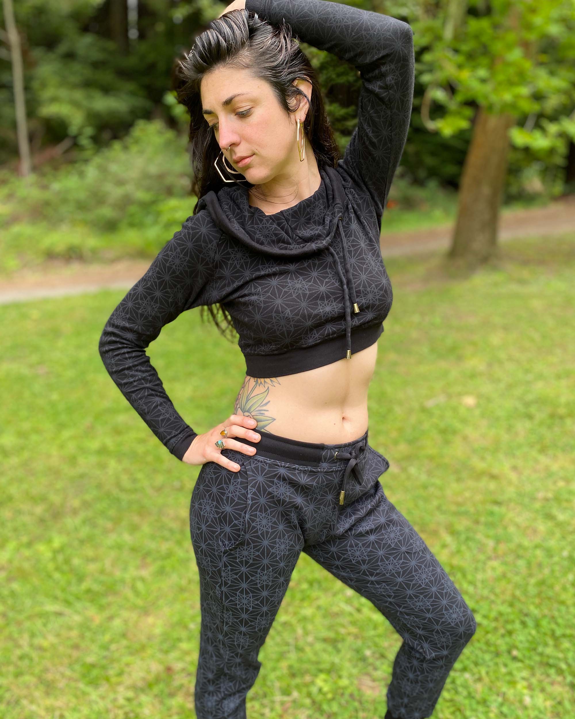 A woman wearing an organic cotton black crop hoodie with geometric print and matching joggers, full front view in an outdoor setting.