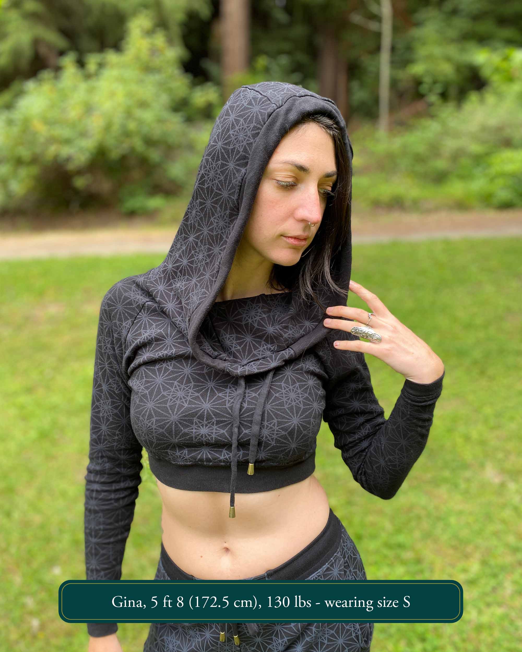 A woman wearing an organic cotton black crop hoodie with geometric print, with matching joggers, front view in a outdoor setting.