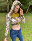 A woman wearing an organic cotton undyed crop hoodie with brown geometric printed fabric and green accents, worn with hood up, right side view.