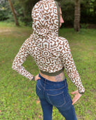 A woman wearing an organic cotton undyed crop hoodie with brown geometric print, worn with hood up, back side view.