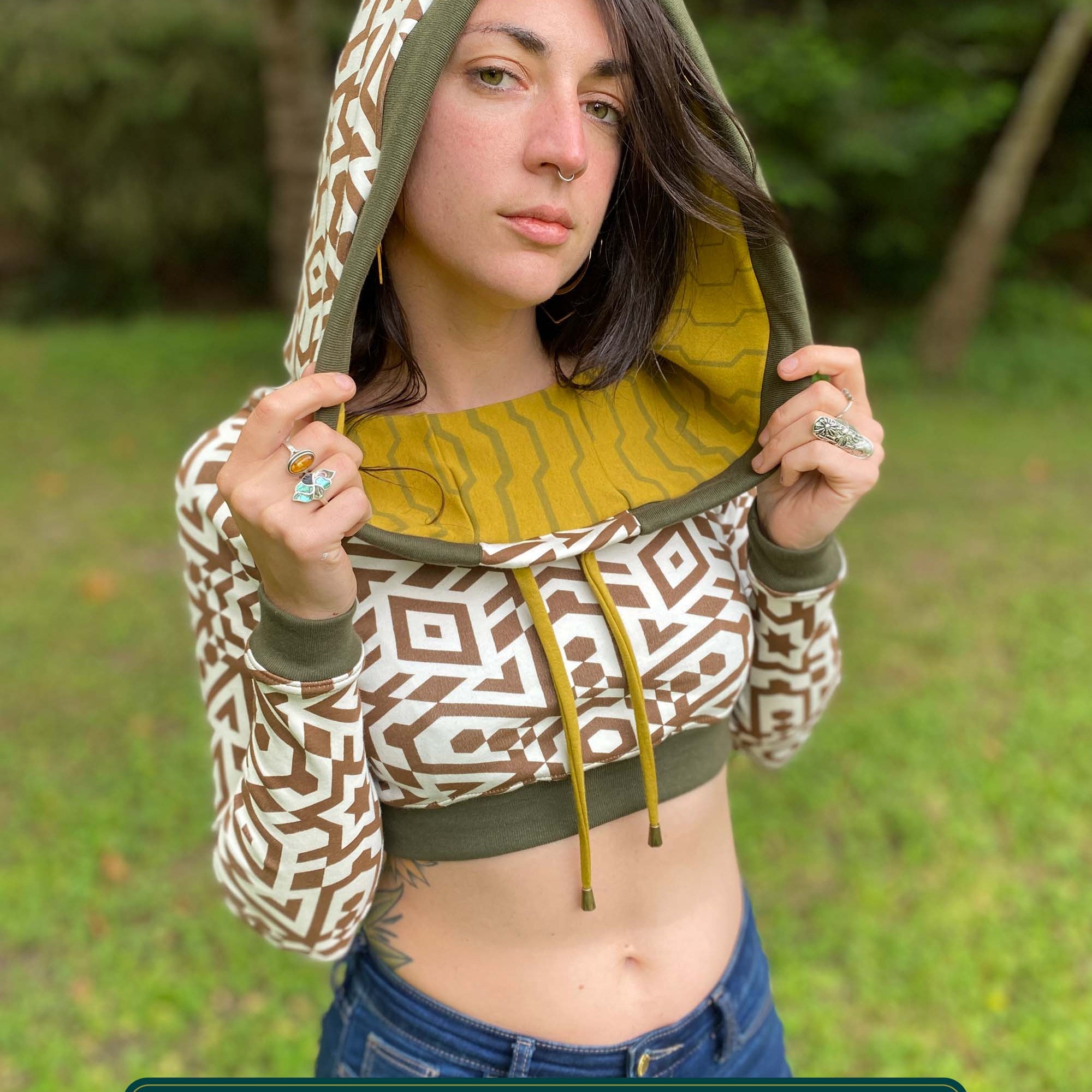 A woman wearing an organic cotton undyed crop hoodie with brown geometric printed fabric and green accents, front view.