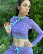 A woman wearing an organic cotton lavender crop hoodie with geometric print, cowl hood and long sleeves, front view.