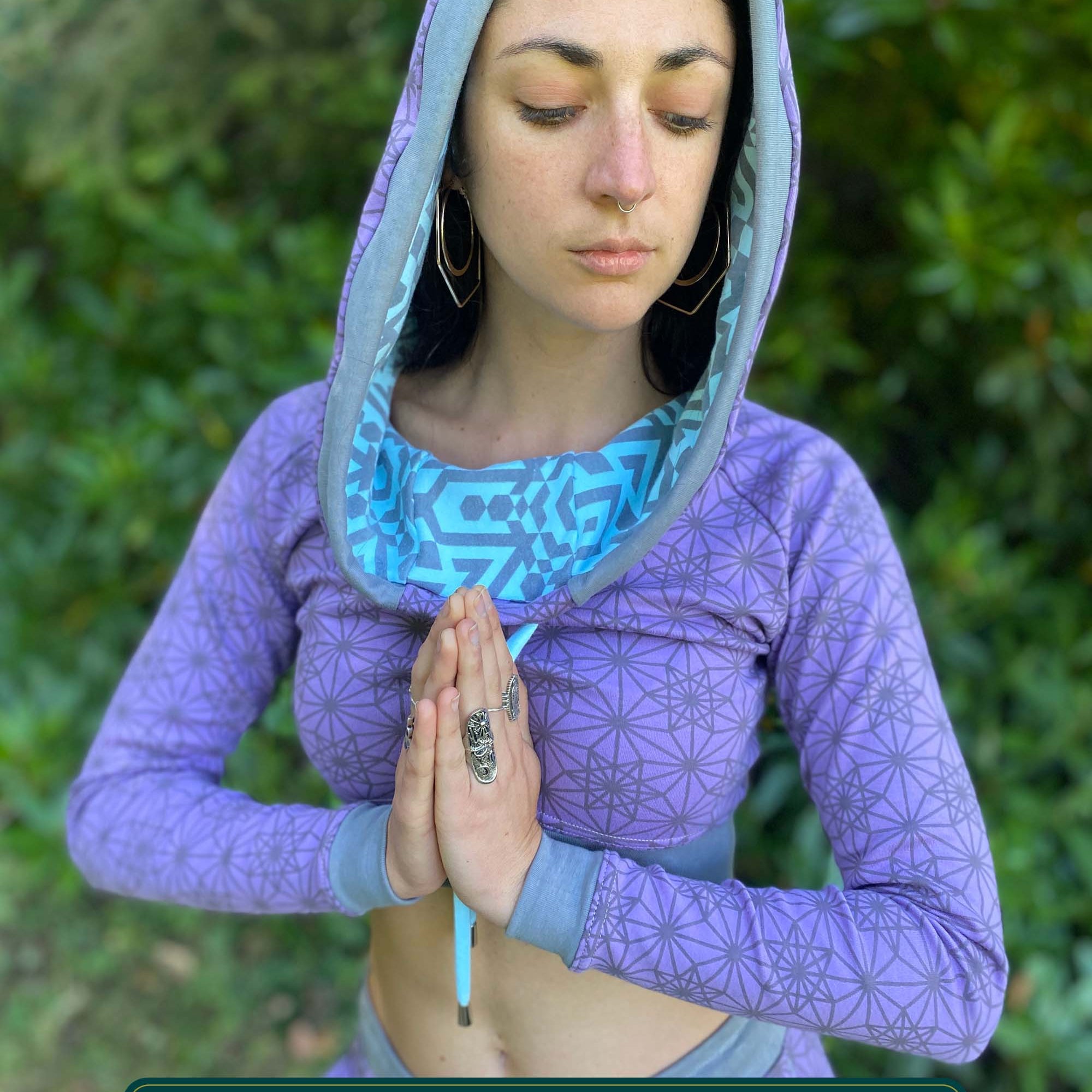 A woman wearing an organic cotton lavender crop hoodie with geometric print, worn with hood up, front view.